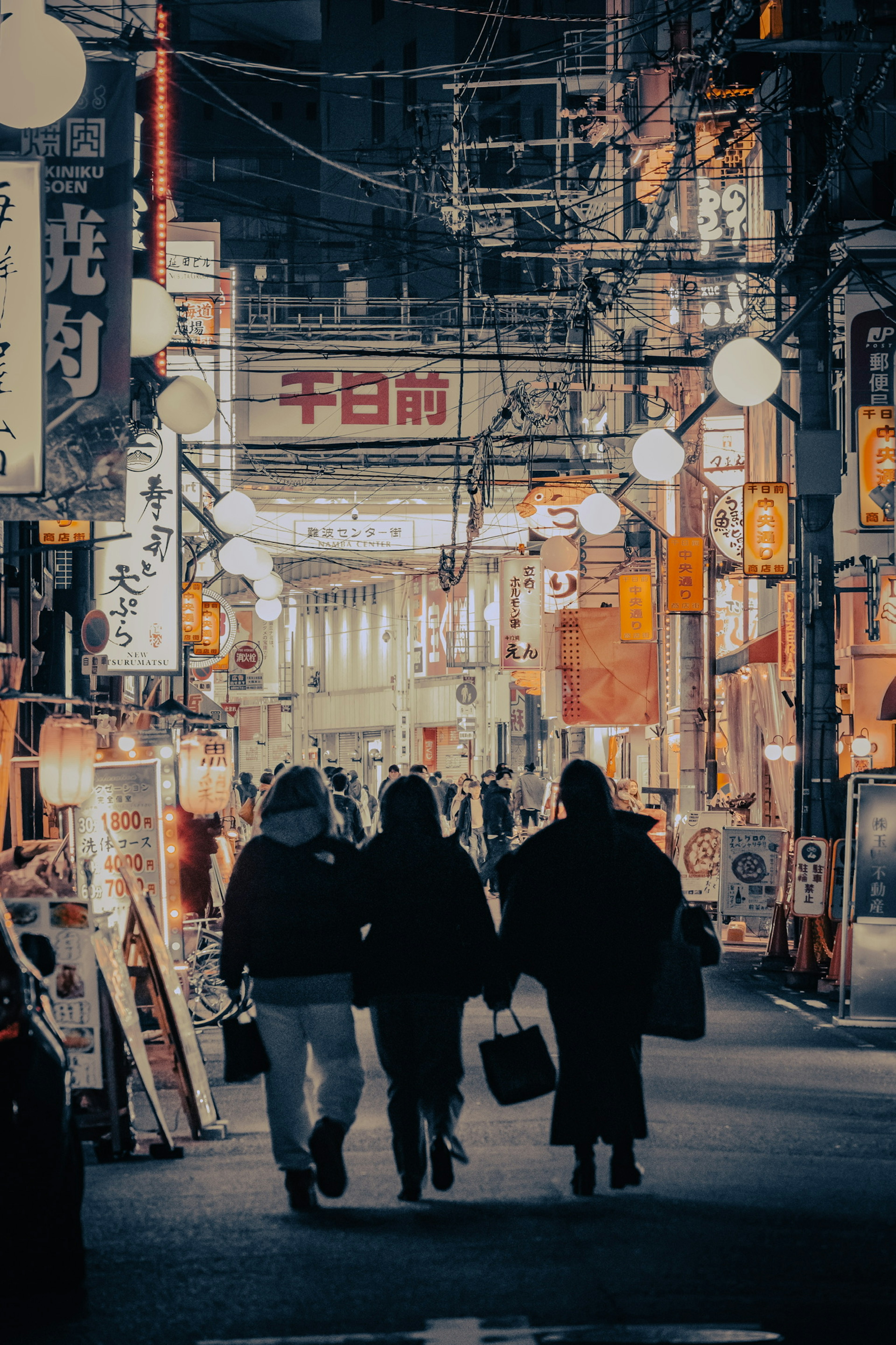 暗い通りを歩く三人のシルエットと明るい看板