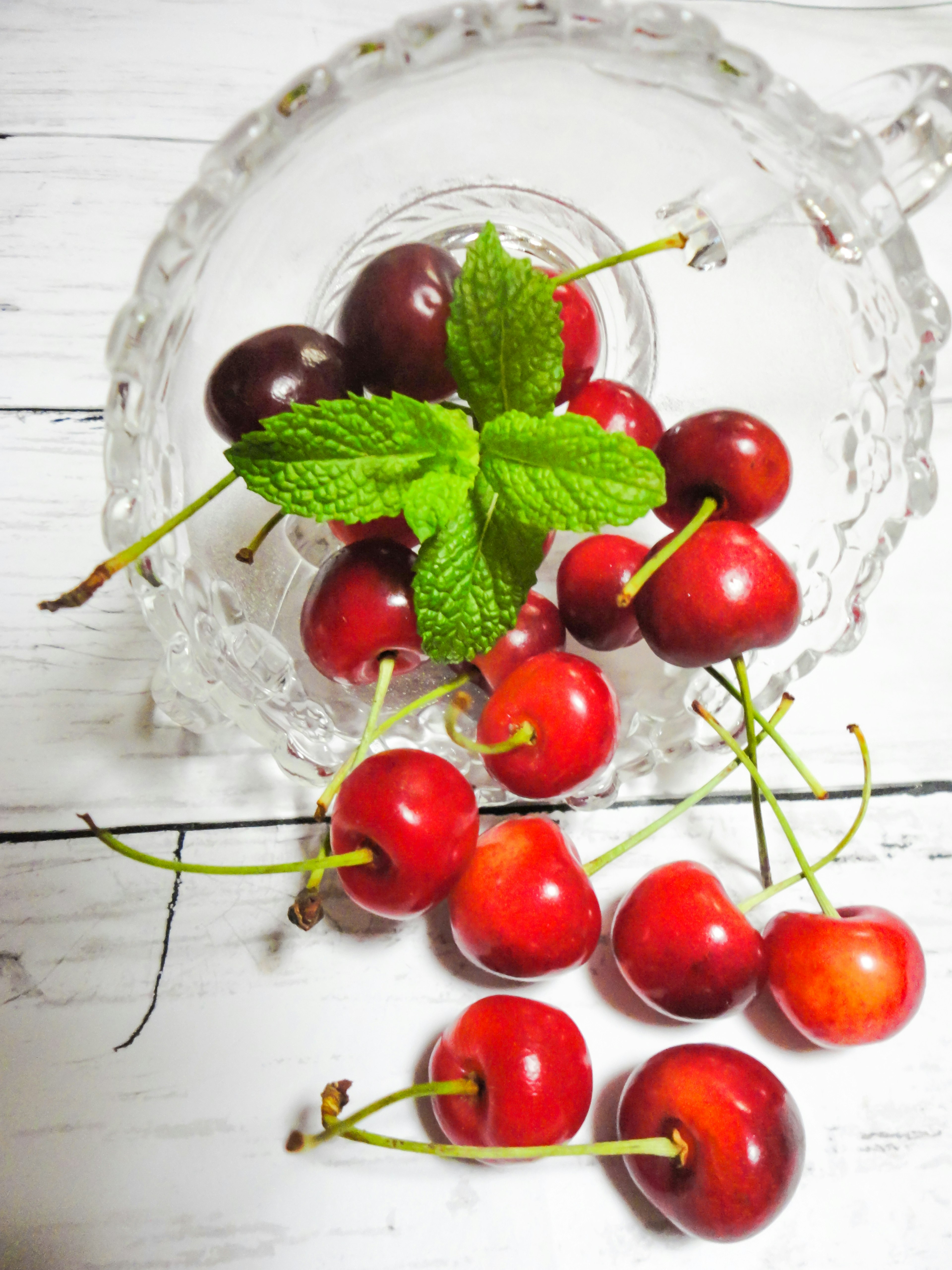 Cerezas rojas con hojas de menta verde en un tazón de vidrio transparente