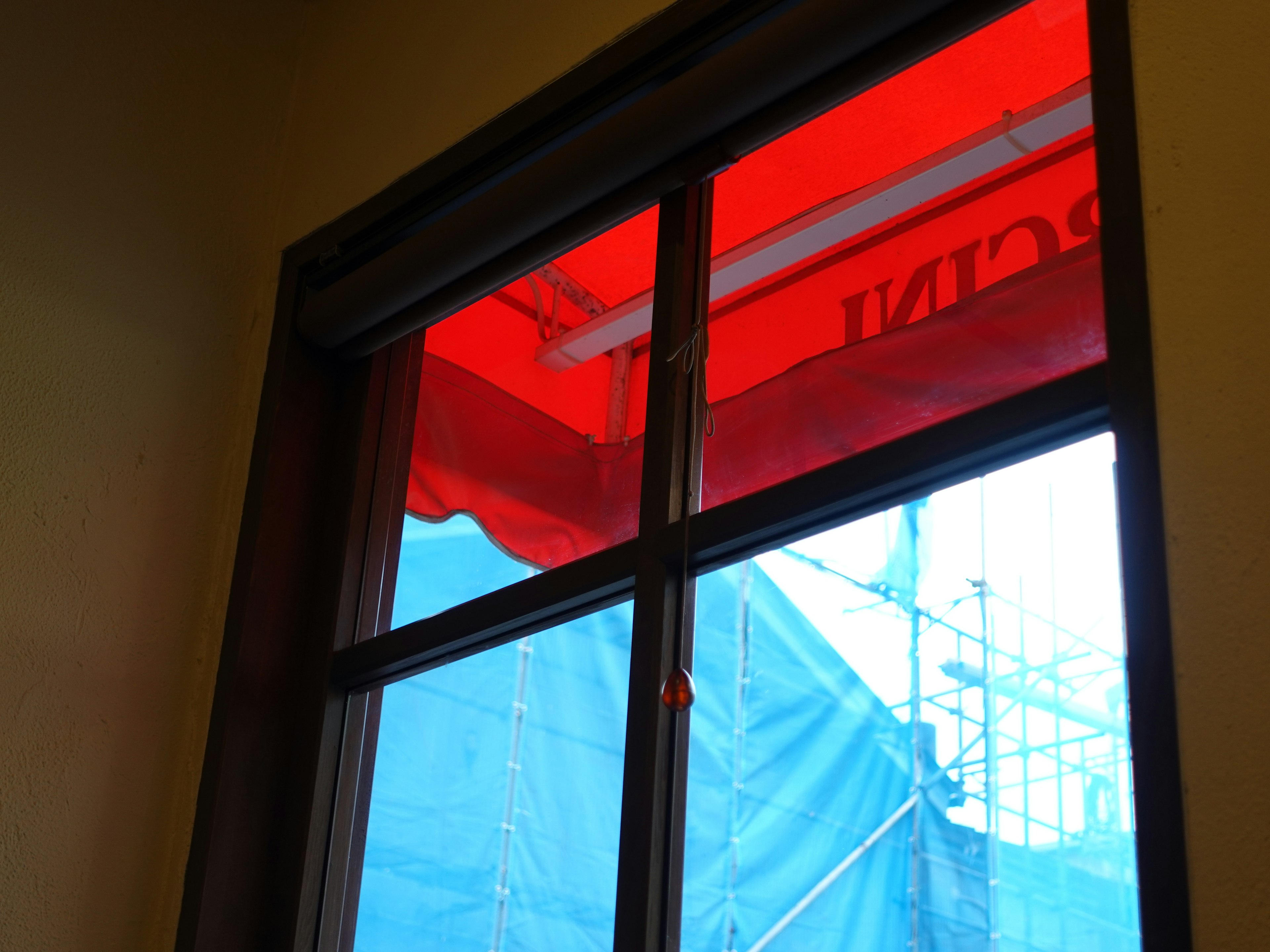 Vista interna di una finestra con un awning rosso e un telo blu all'esterno