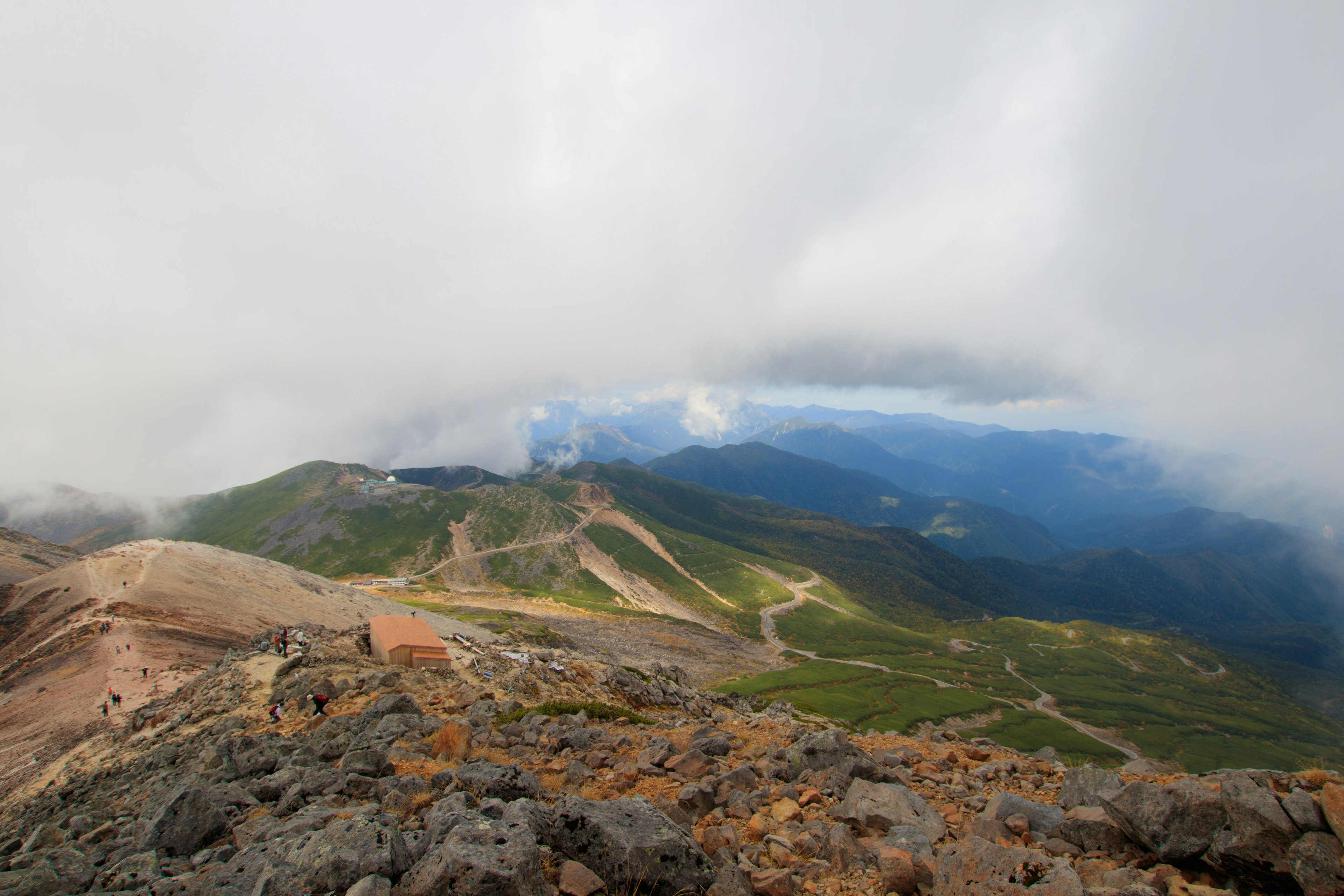 Une vue depuis le sommet de la montagne couverte de nuages montrant des collines vertes et un terrain rocheux