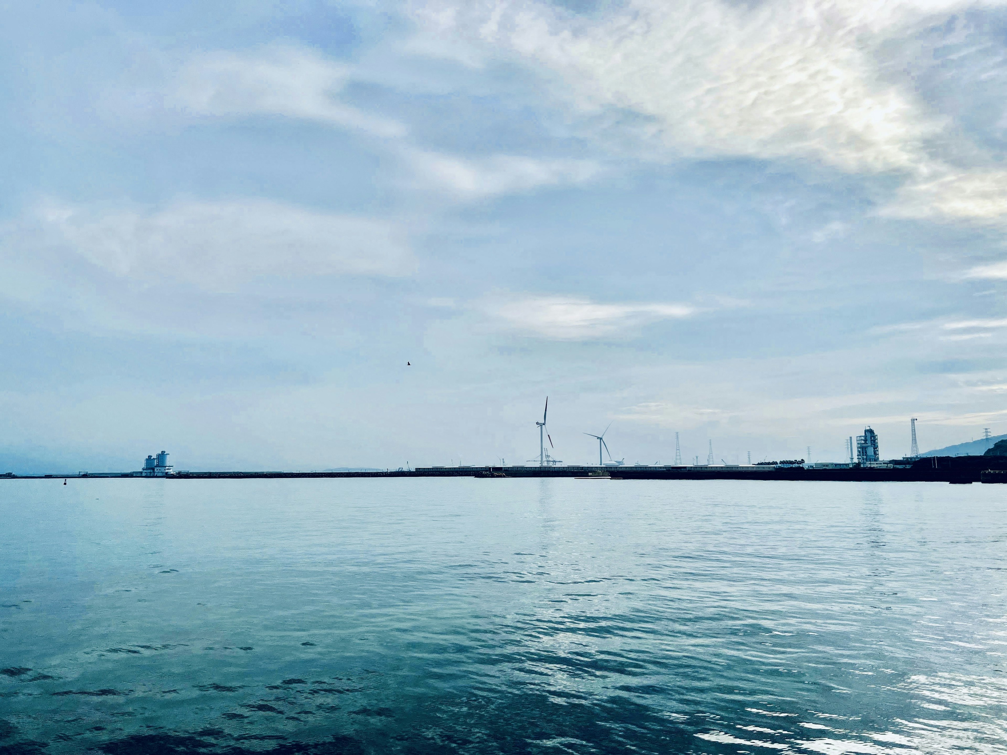 Calm sea with blue sky and visible wind turbines