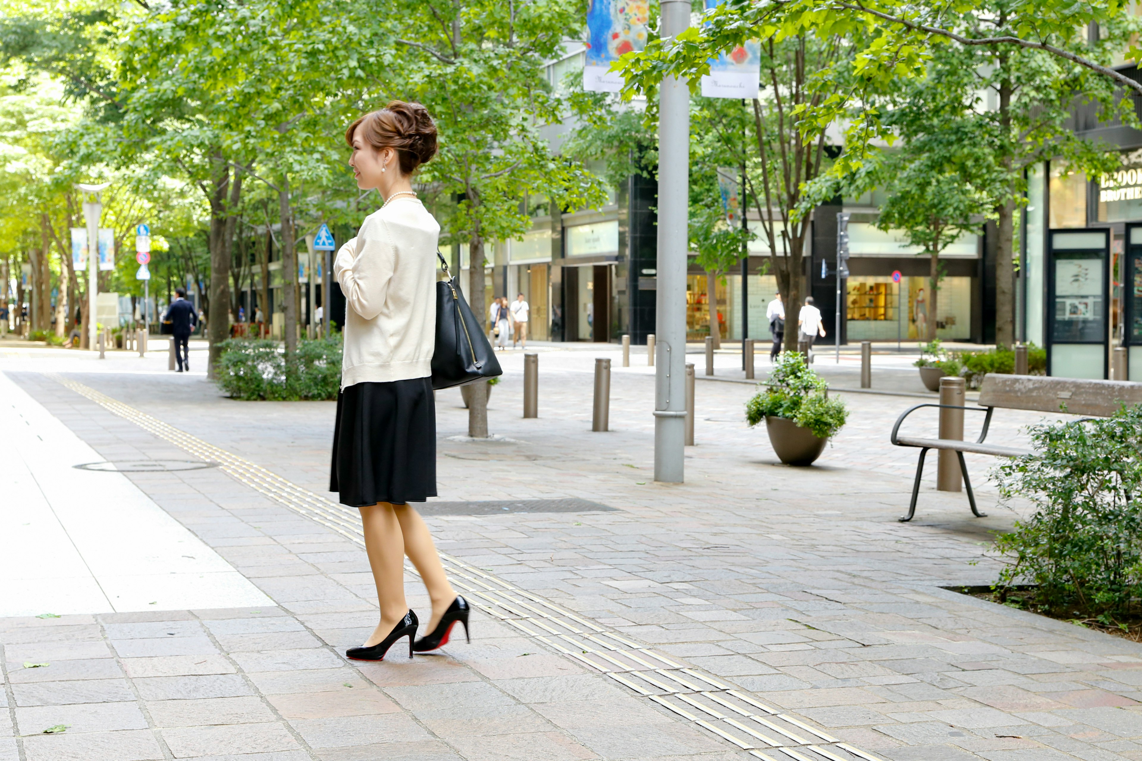 A woman walking in an urban setting with green trees and shops