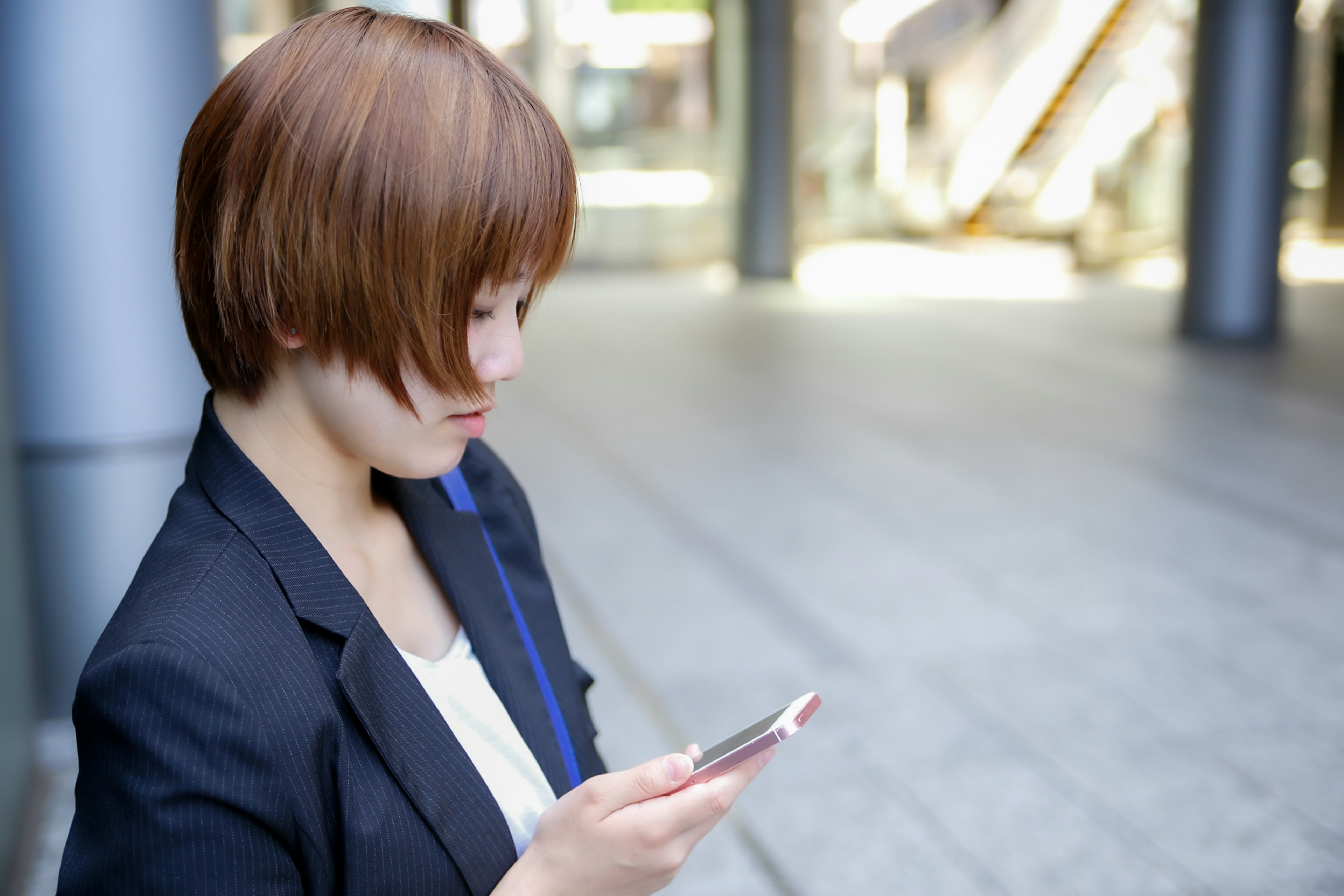 Seorang wanita berjas menggunakan smartphone di luar ruangan