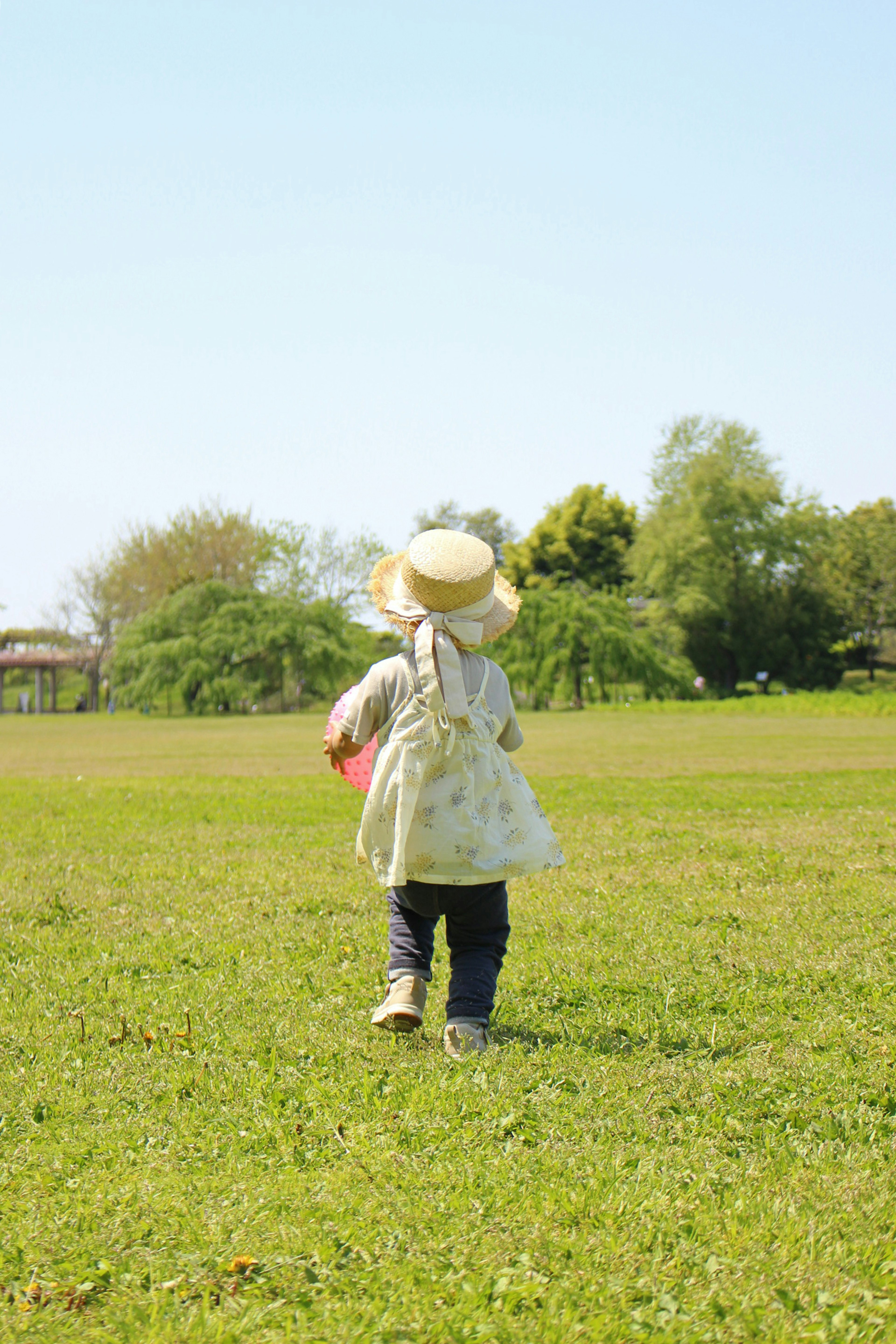 Seorang anak mengenakan topi berjalan di lapangan rumput di bawah langit biru