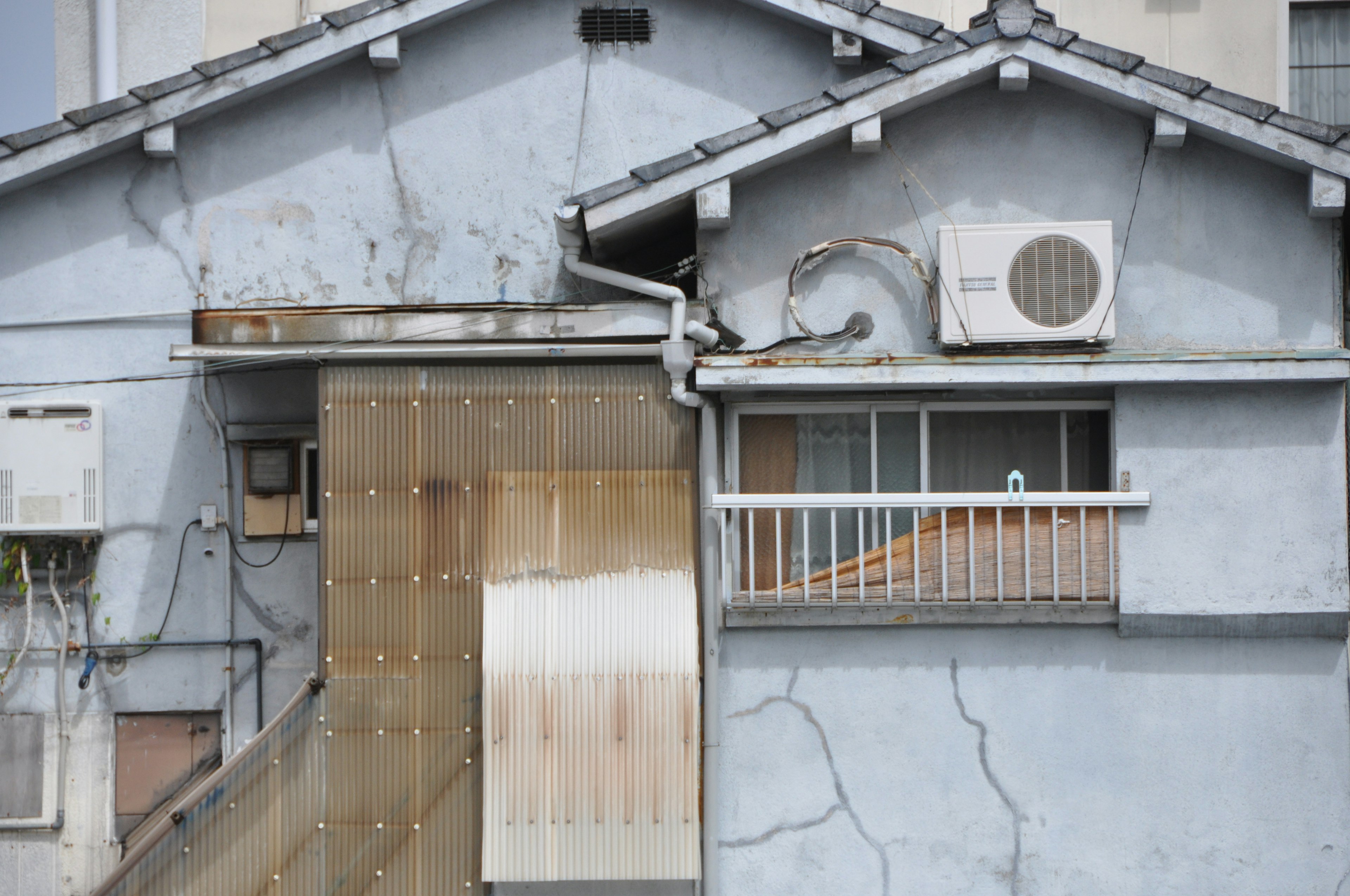 Exterior de una casa antigua mostrando grietas y una unidad de aire acondicionado