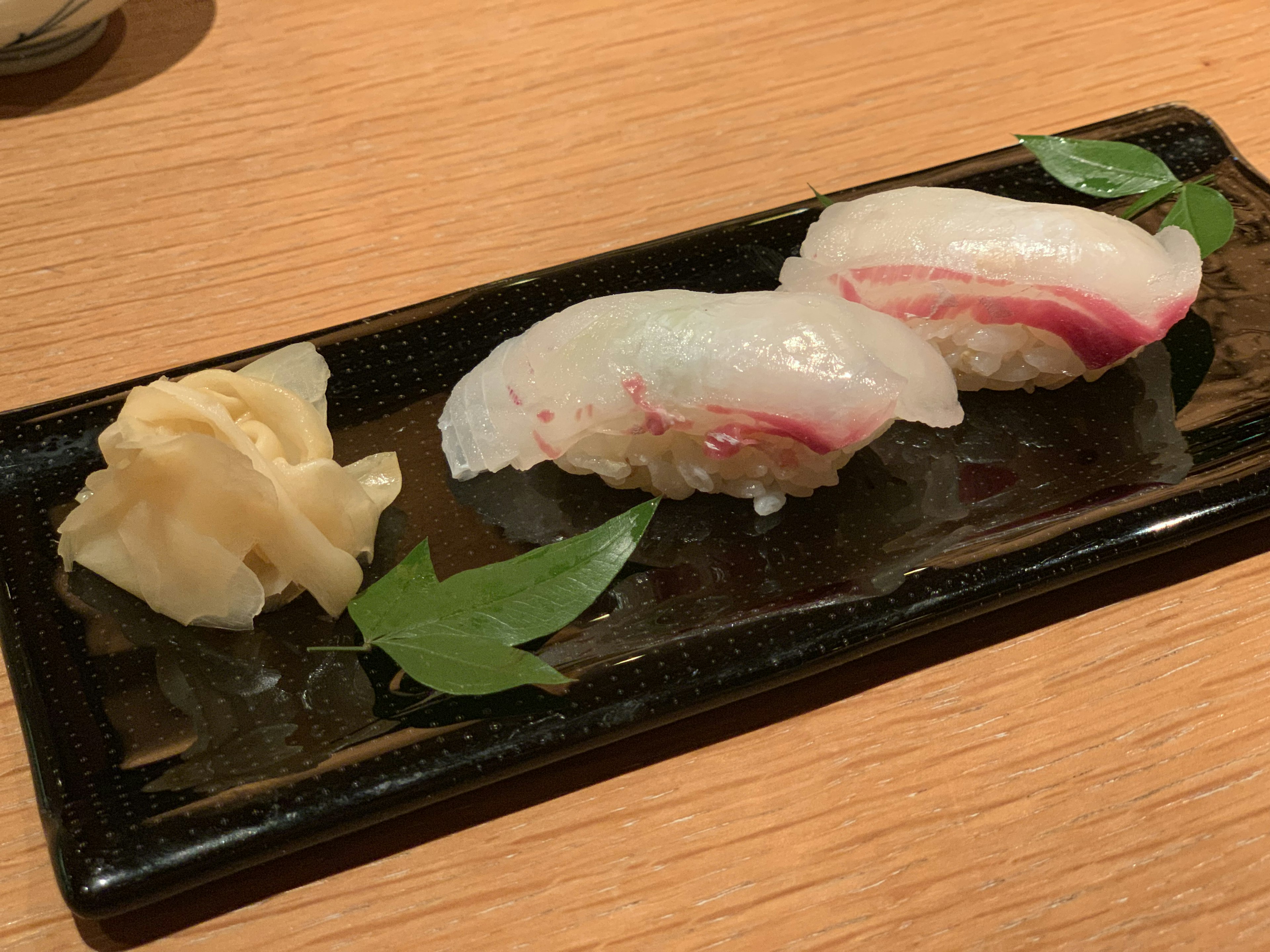 Sushi servido en un plato negro con jengibre encurtido al lado