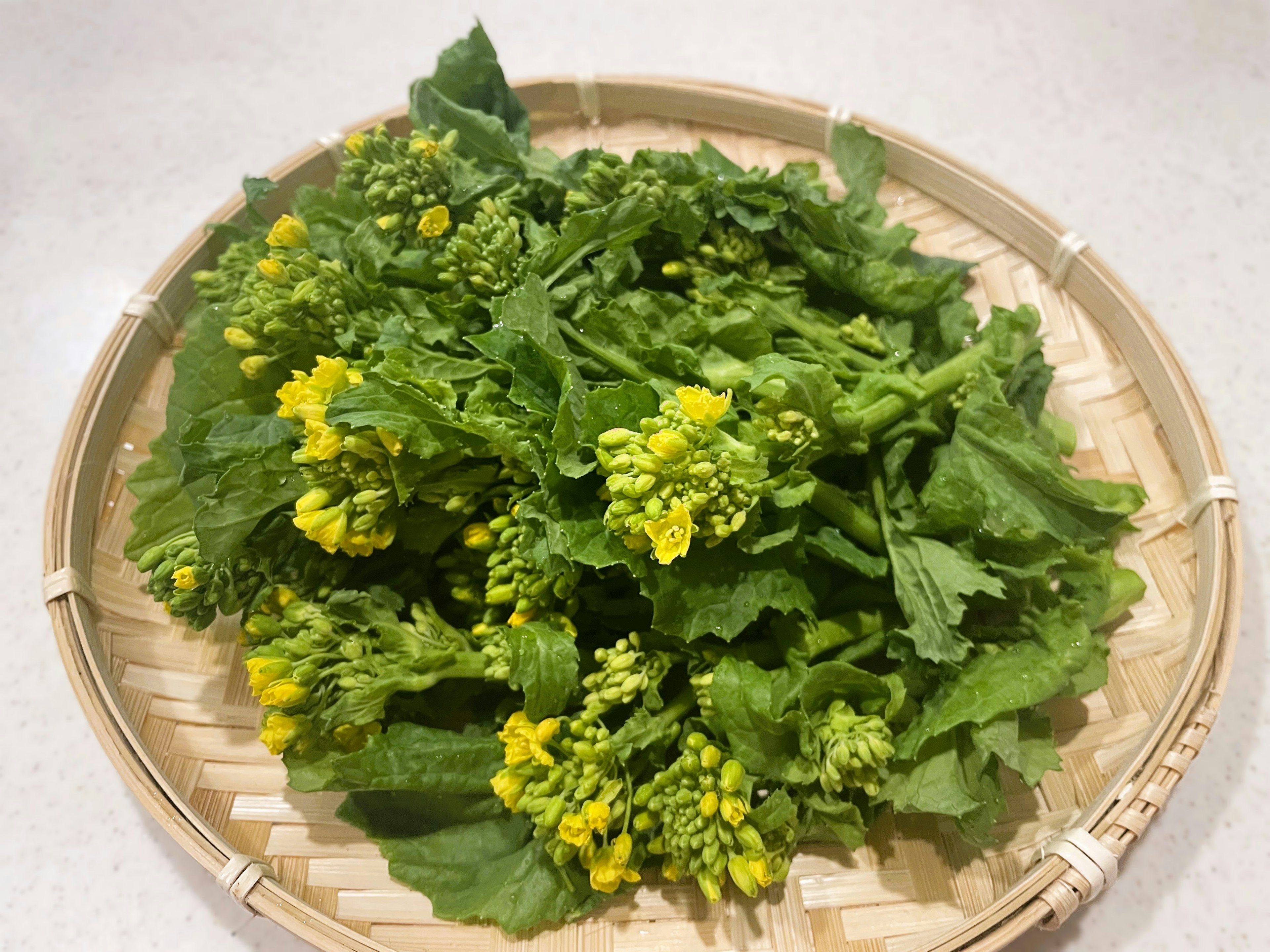 Feuilles vertes fraîches de colza avec des fleurs jaunes disposées dans une assiette en bambou