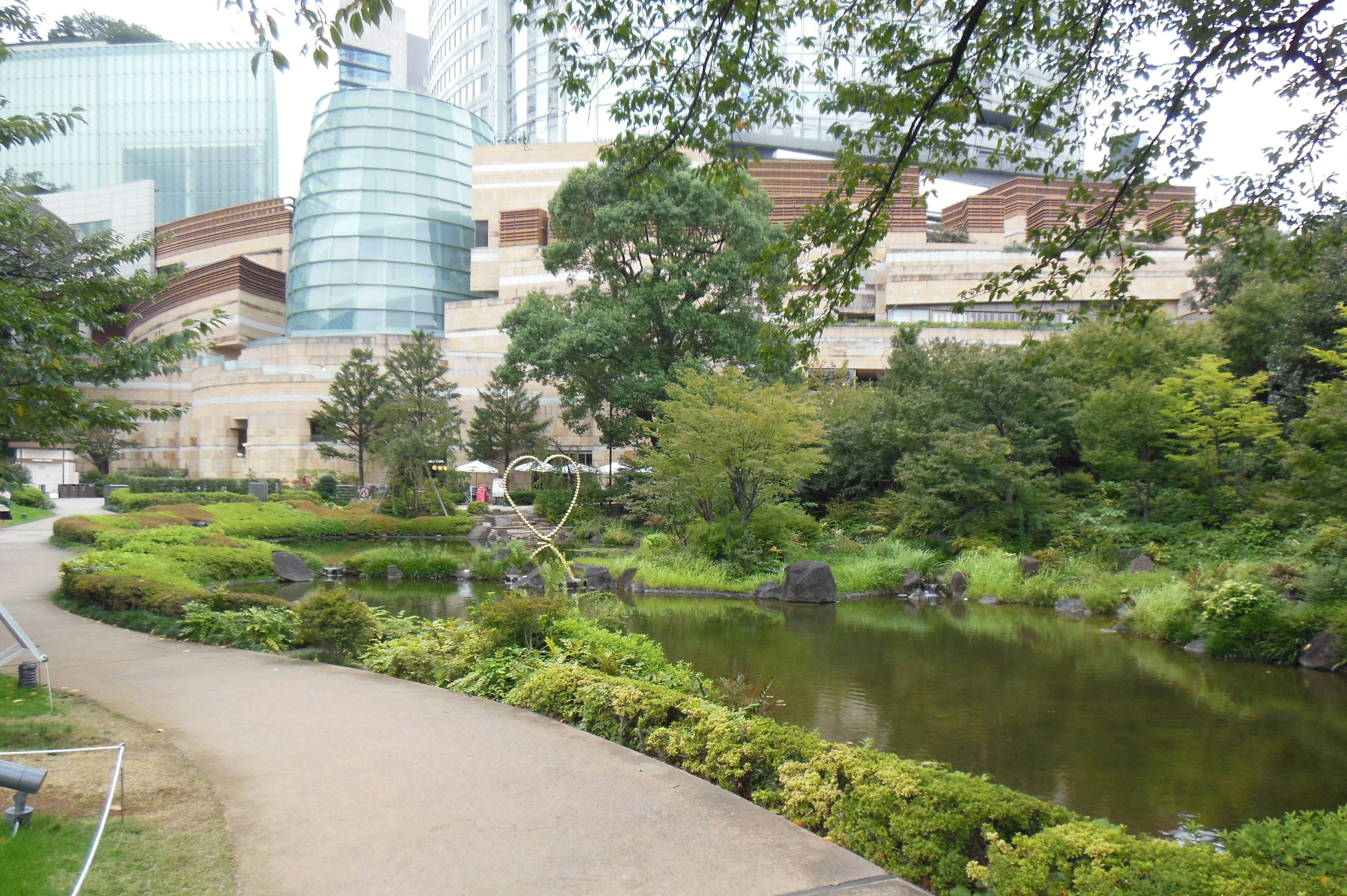 Paisaje de parque exuberante con un estanque y edificios modernos al fondo