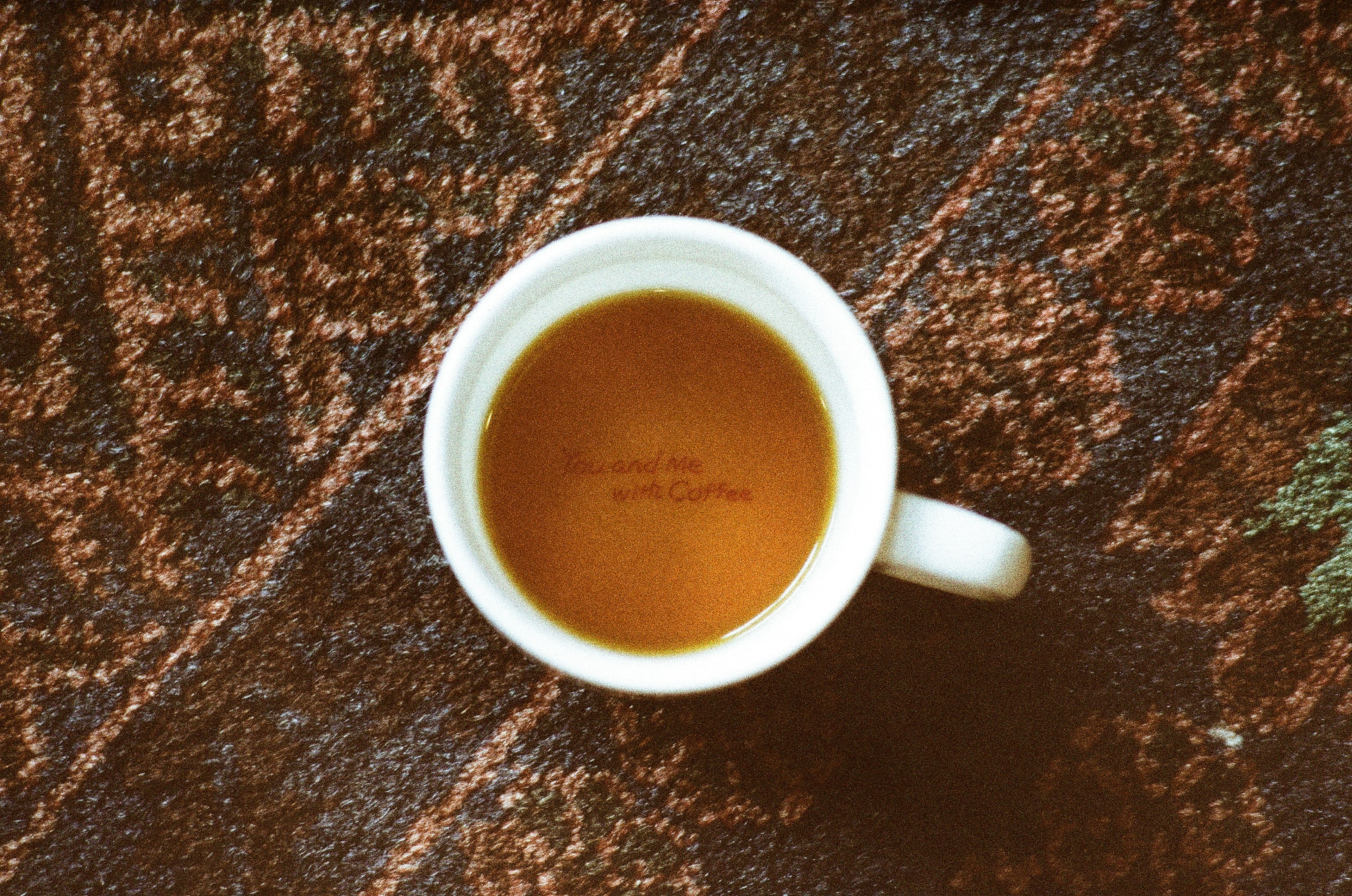 Una taza blanca de café colocada sobre una alfombra marrón