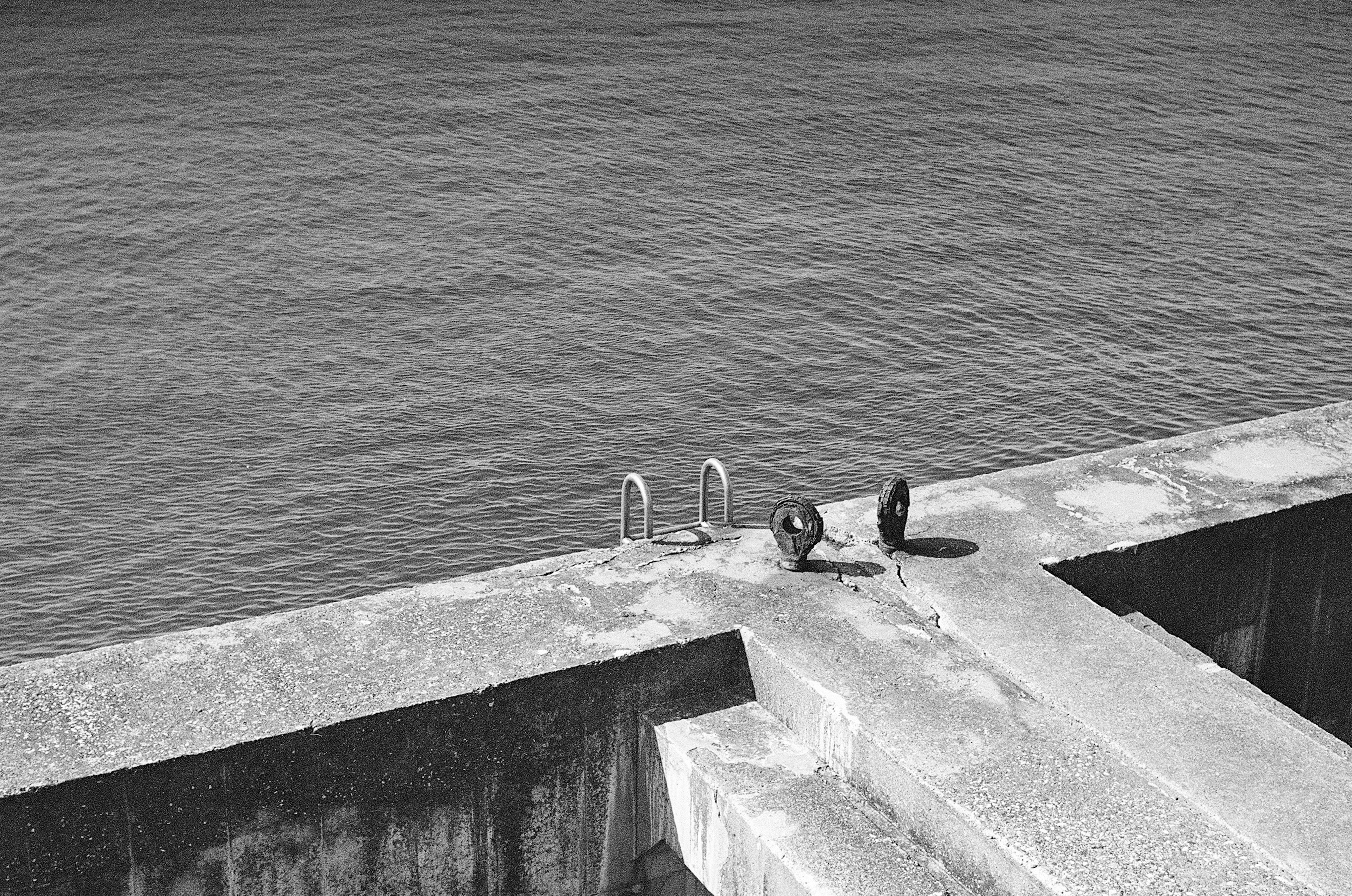 Foto in bianco e nero di un molo di cemento con scarpe posate sopra la superficie dell'acqua