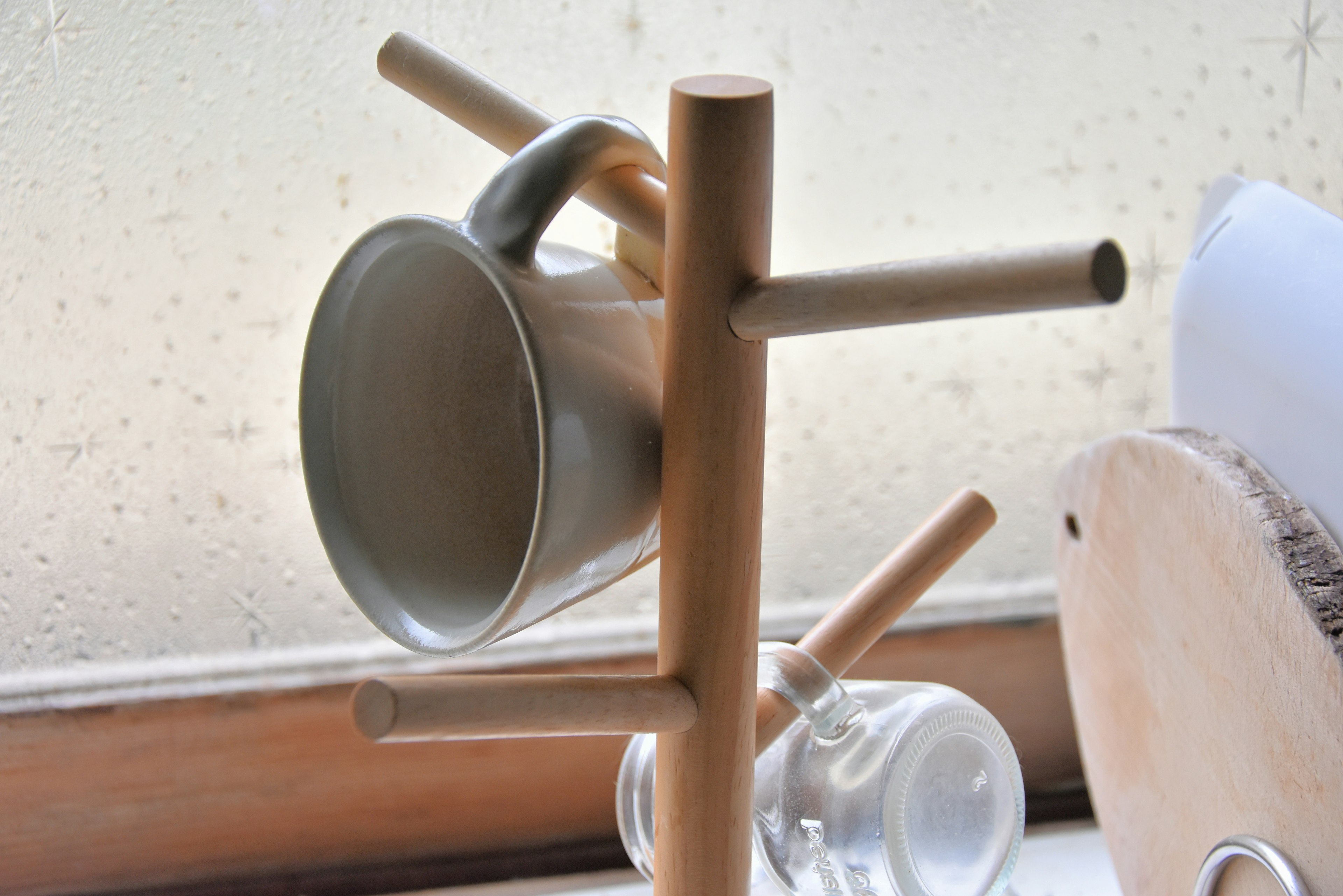 White mug hanging on a wooden cup stand with a glass container nearby