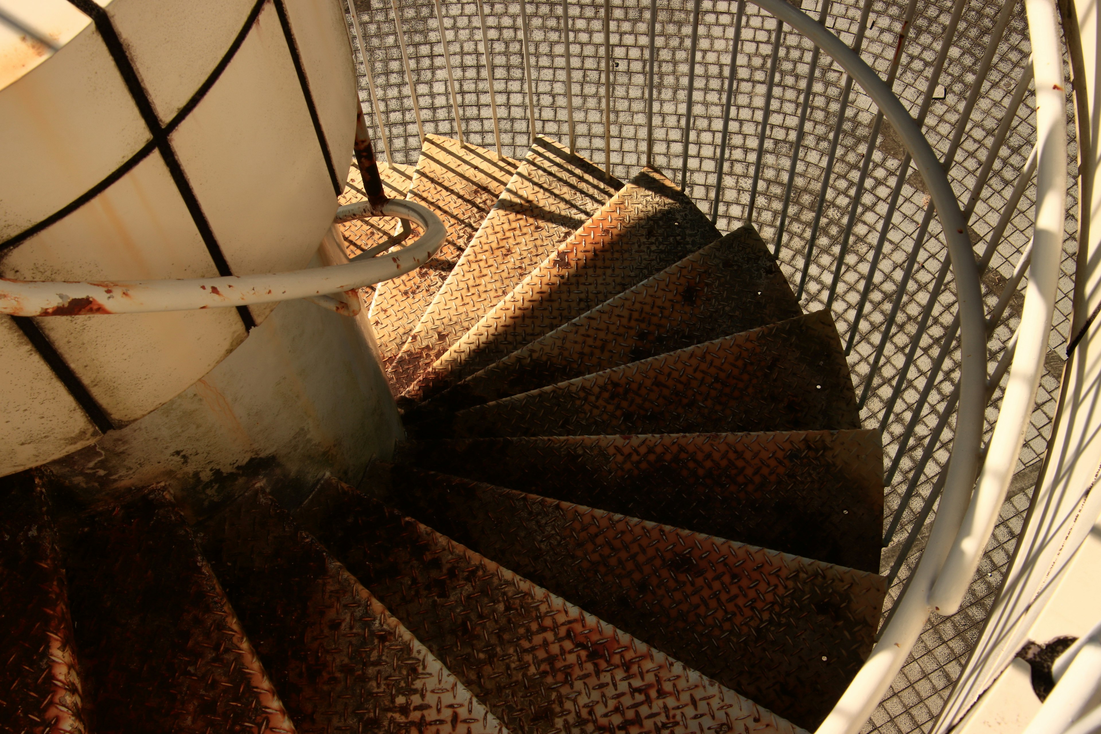 Image d'un escalier en colimaçon vu d'en haut avec métal rouillé et garde-corps en treillis