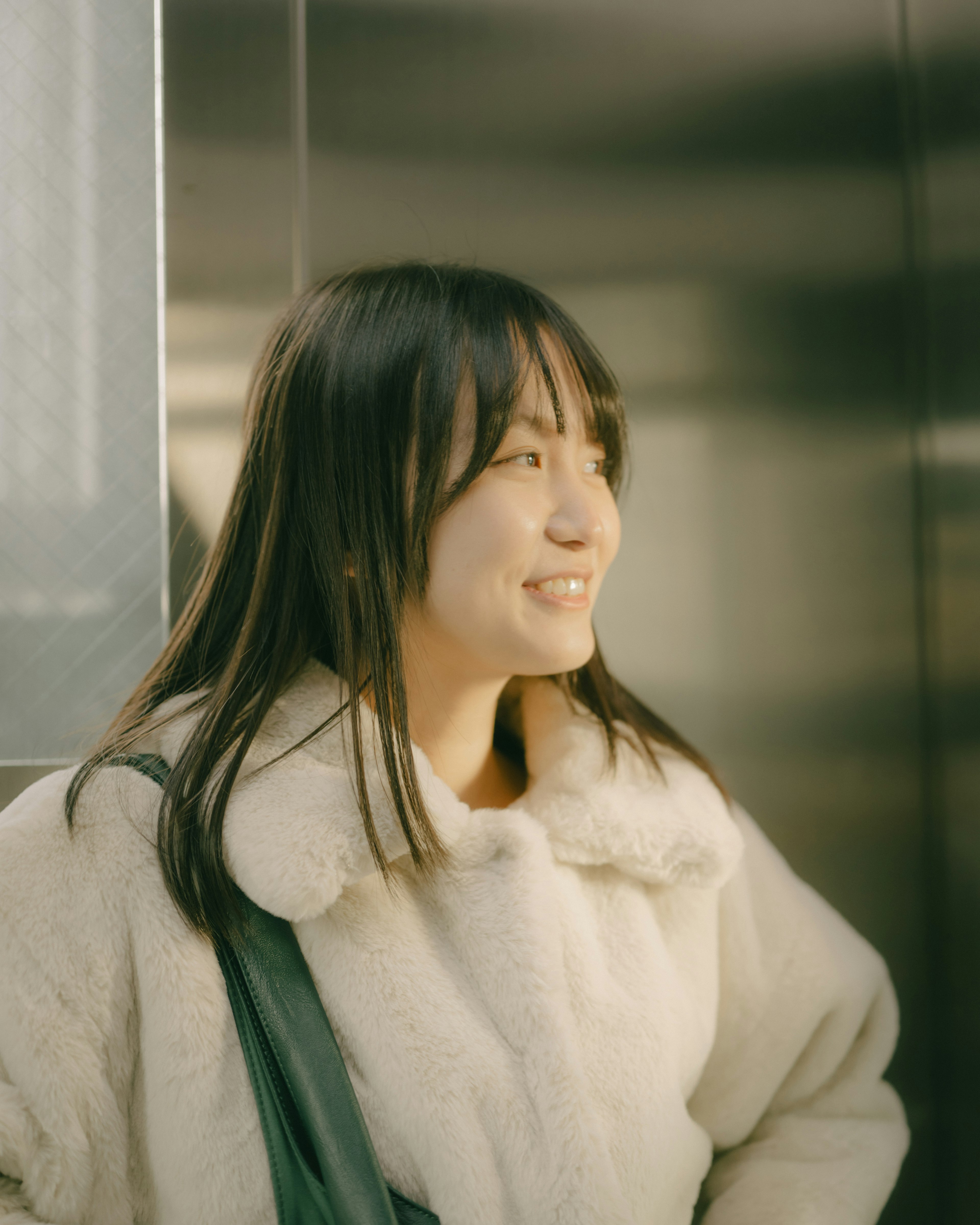 A woman smiling inside an elevator wearing a white coat