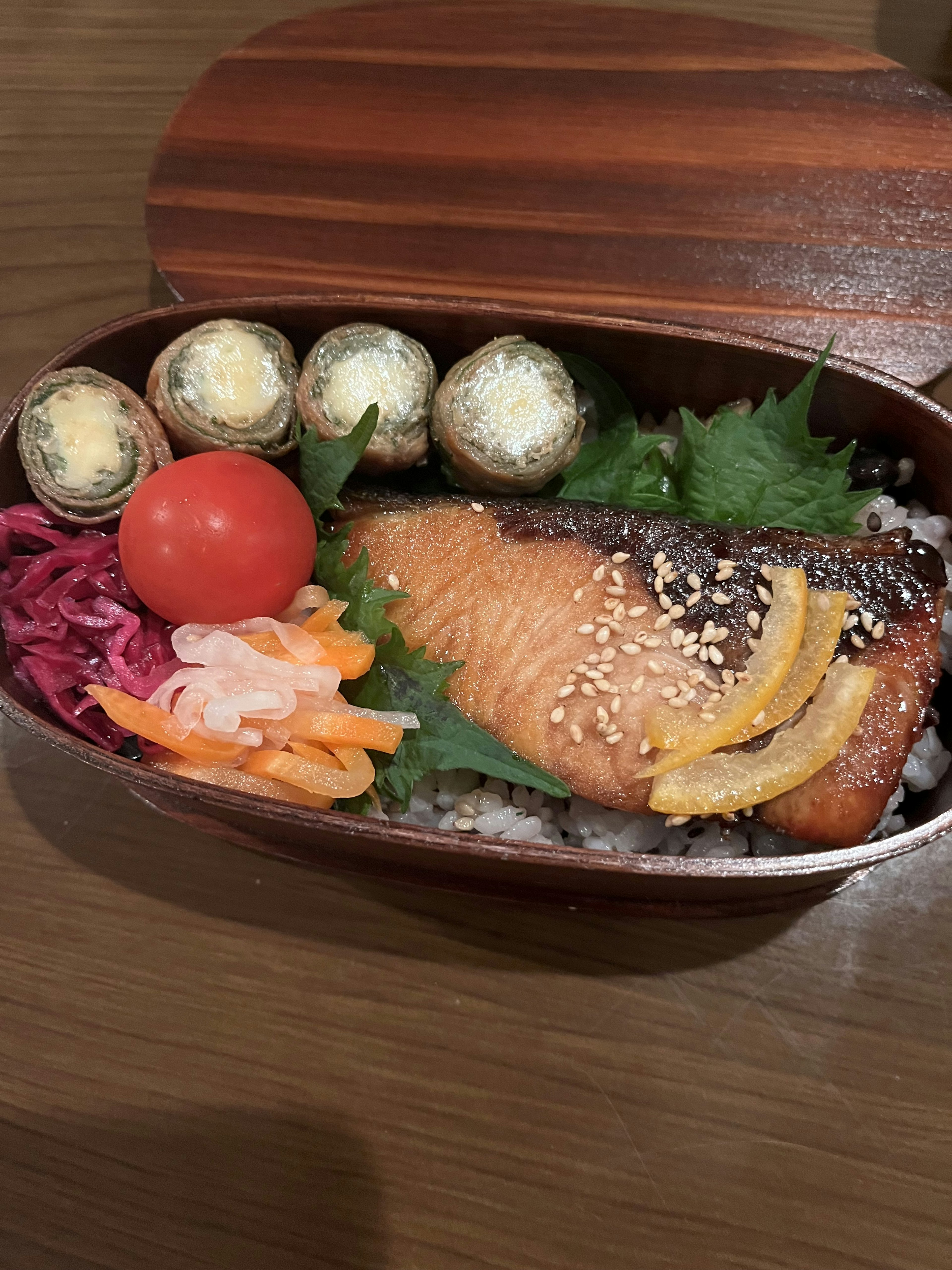 Bento box featuring grilled salmon fillet topped with lemon and sesame served with fresh vegetables