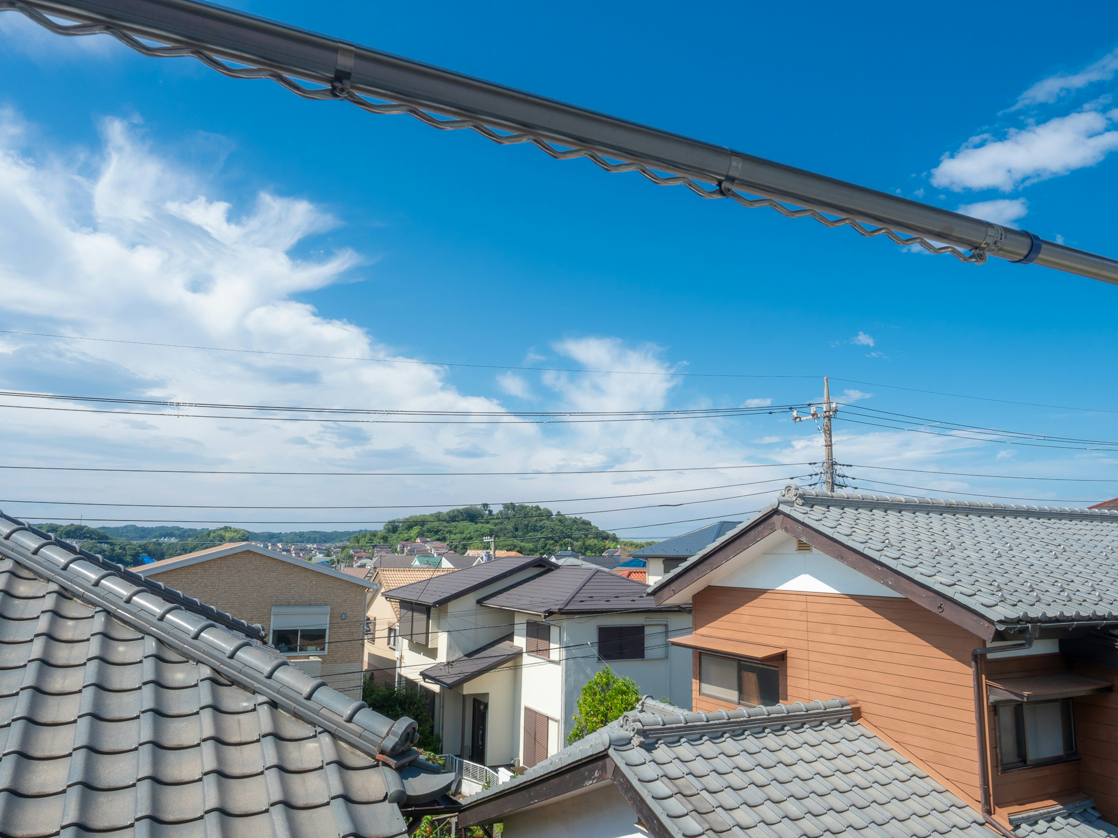 青空と雲が広がる中、住宅街の屋根が見える風景