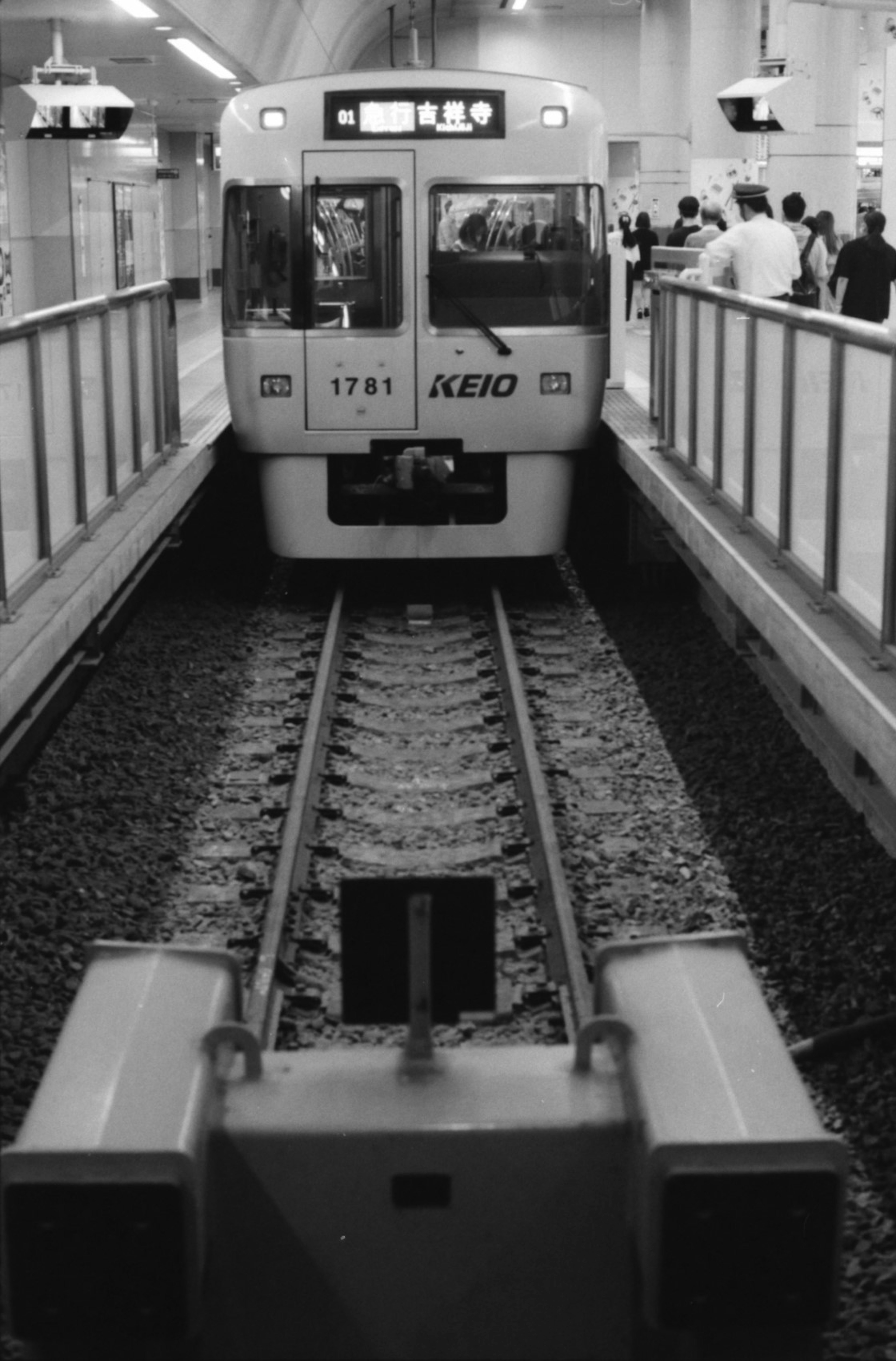 Immagine in bianco e nero di un treno in stazione con passeggeri in attesa