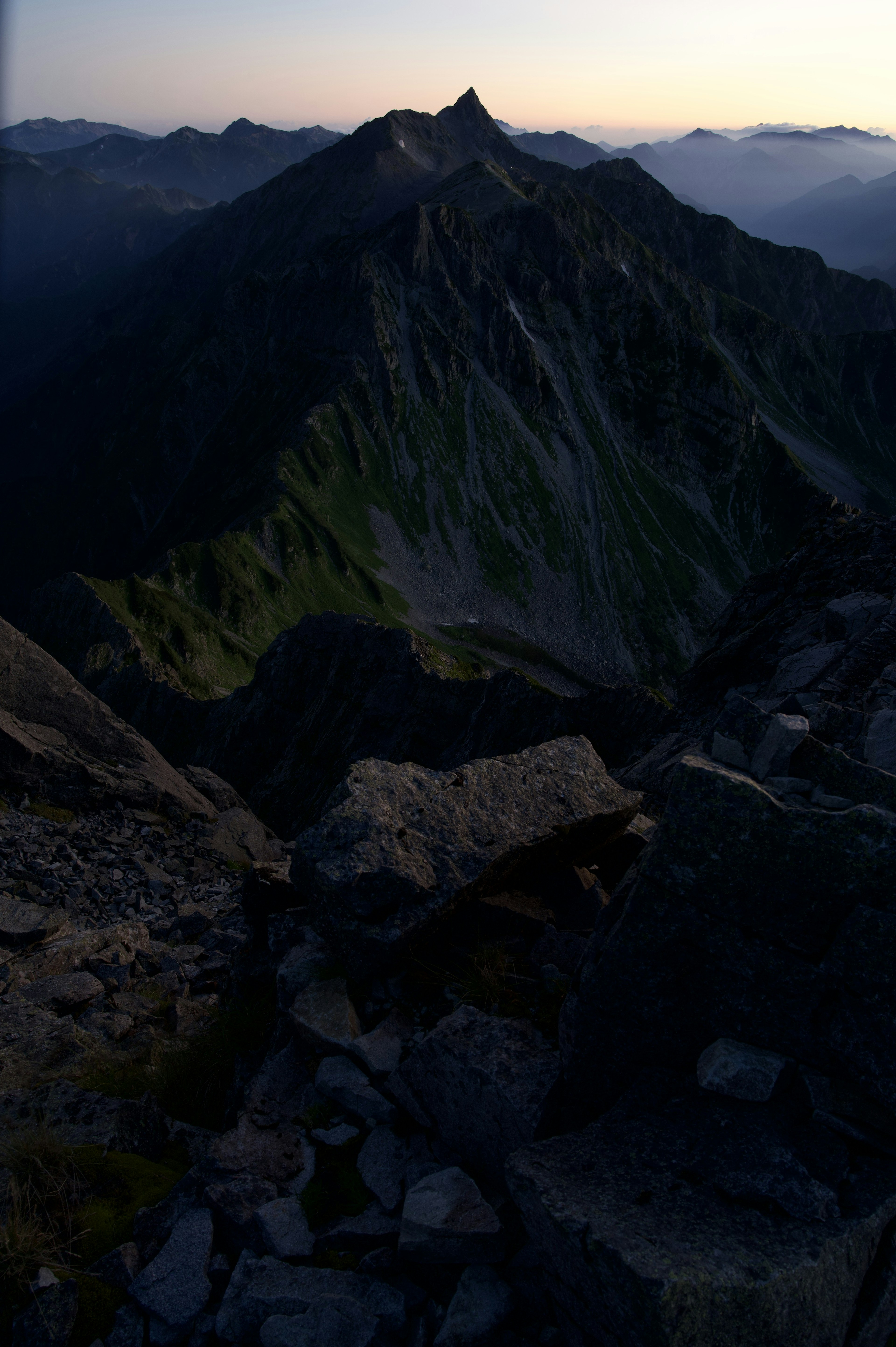 Vue depuis un sommet de montagne sombre montrant des pentes vertes et des rochers