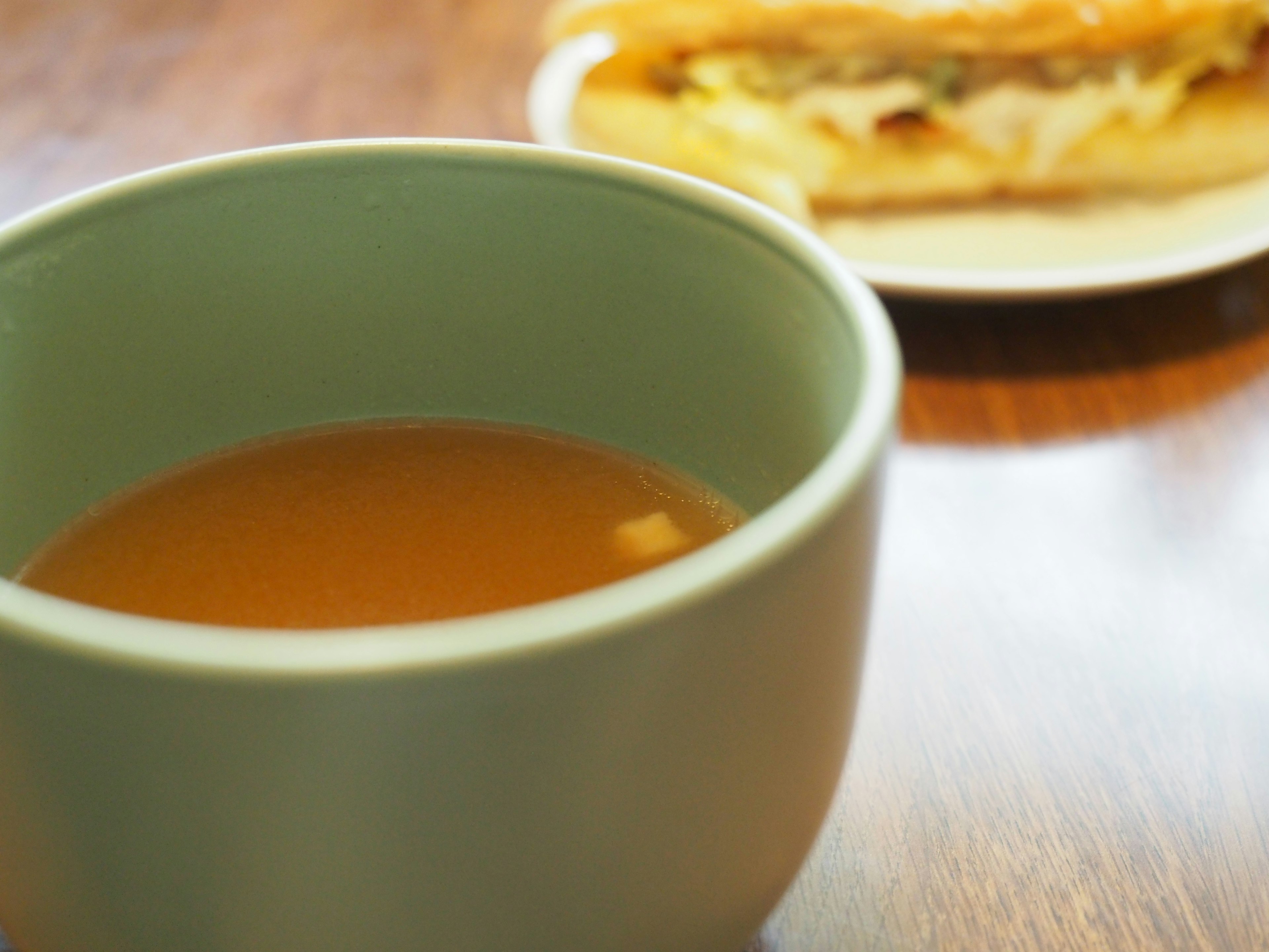 A green bowl with tea and a sandwich on a plate in the background