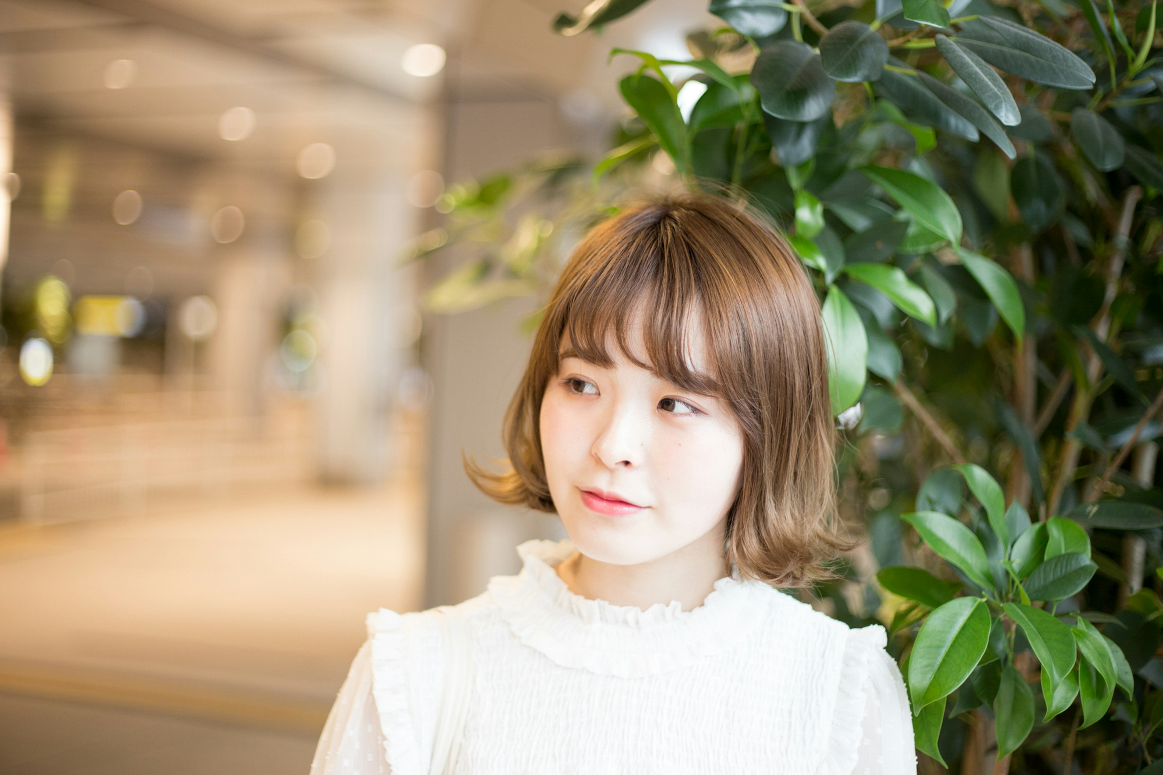 Femme jeune portant une robe blanche souriant devant des plantes vertes