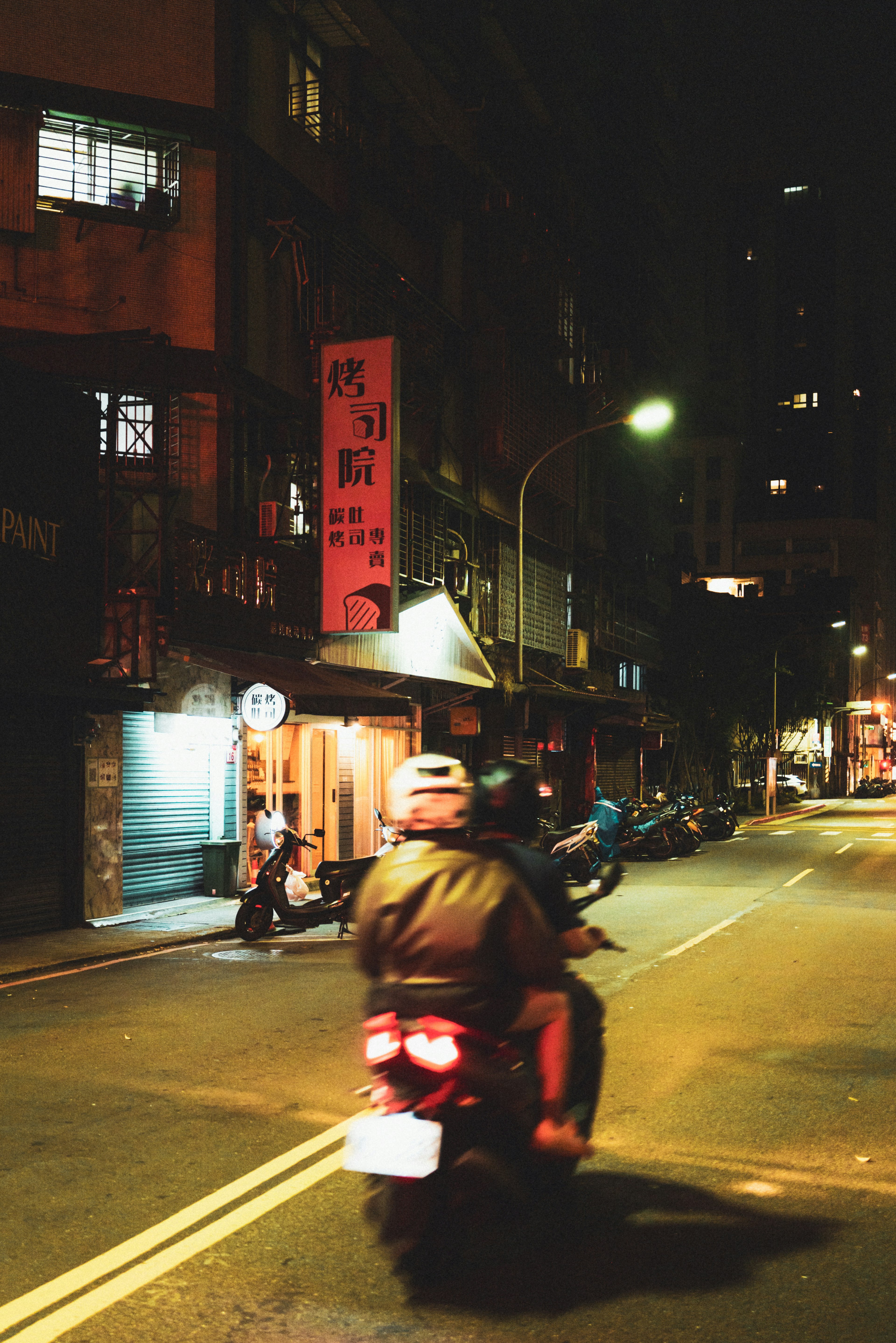 夜の街を走るバイクとその後ろにある店の看板