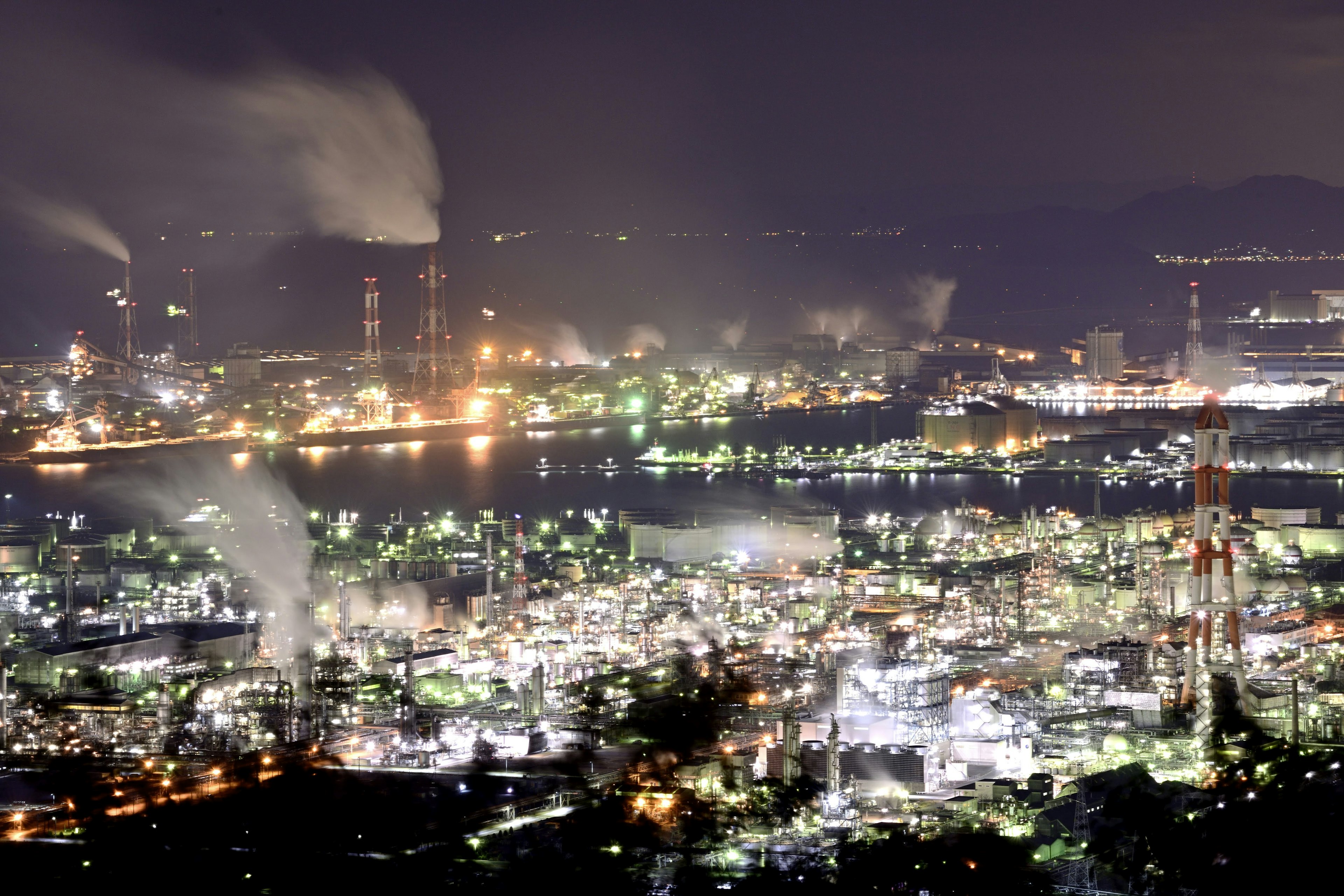 Vista nocturna de una zona industrial con luces brillantes y humo de fábricas