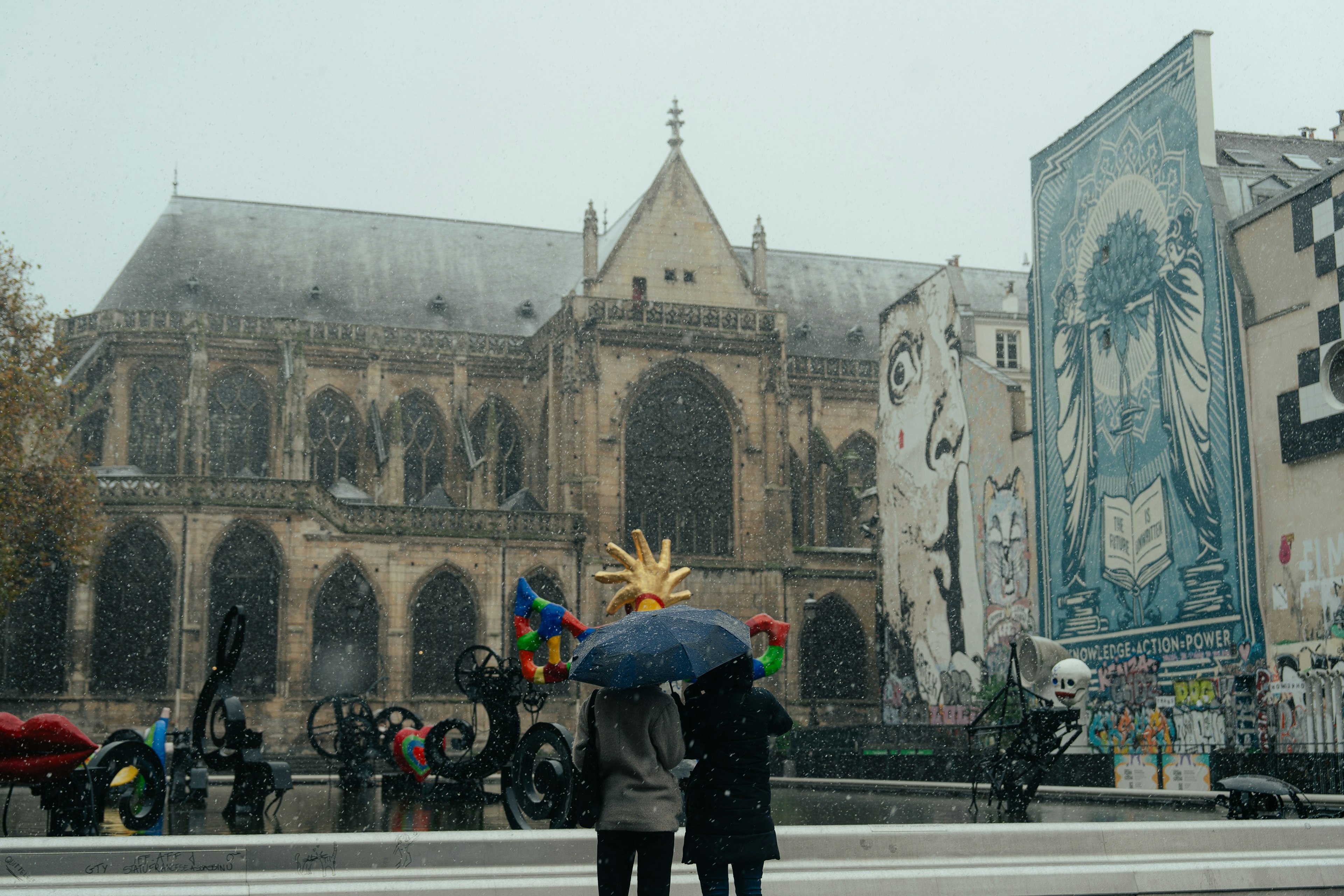 Zwei Personen mit einem Regenschirm im Schnee vor einer schönen Kirche und einem Wandgemälde im Hintergrund