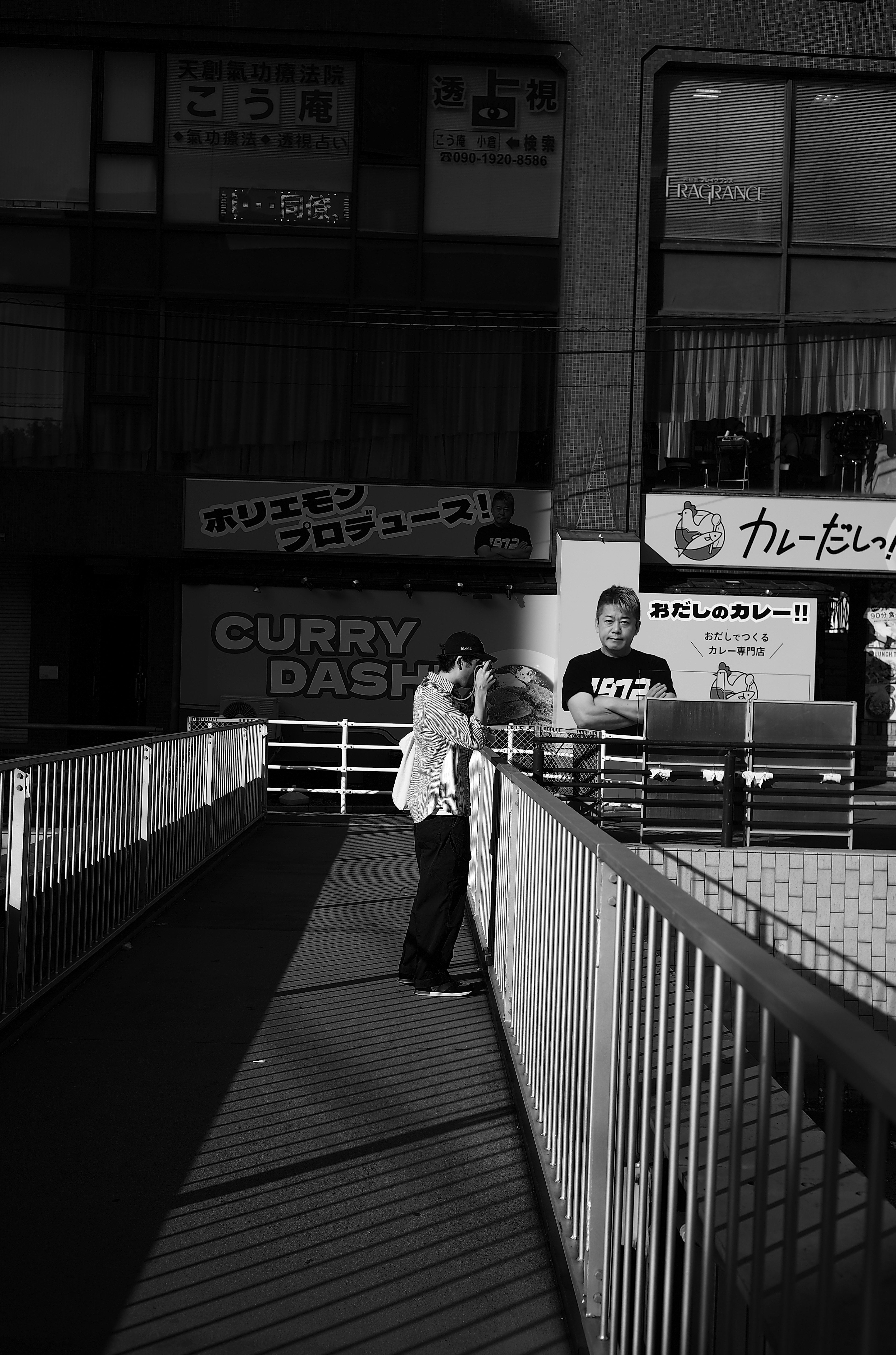 A person holding a camera in a black and white urban scene with a curry shop sign