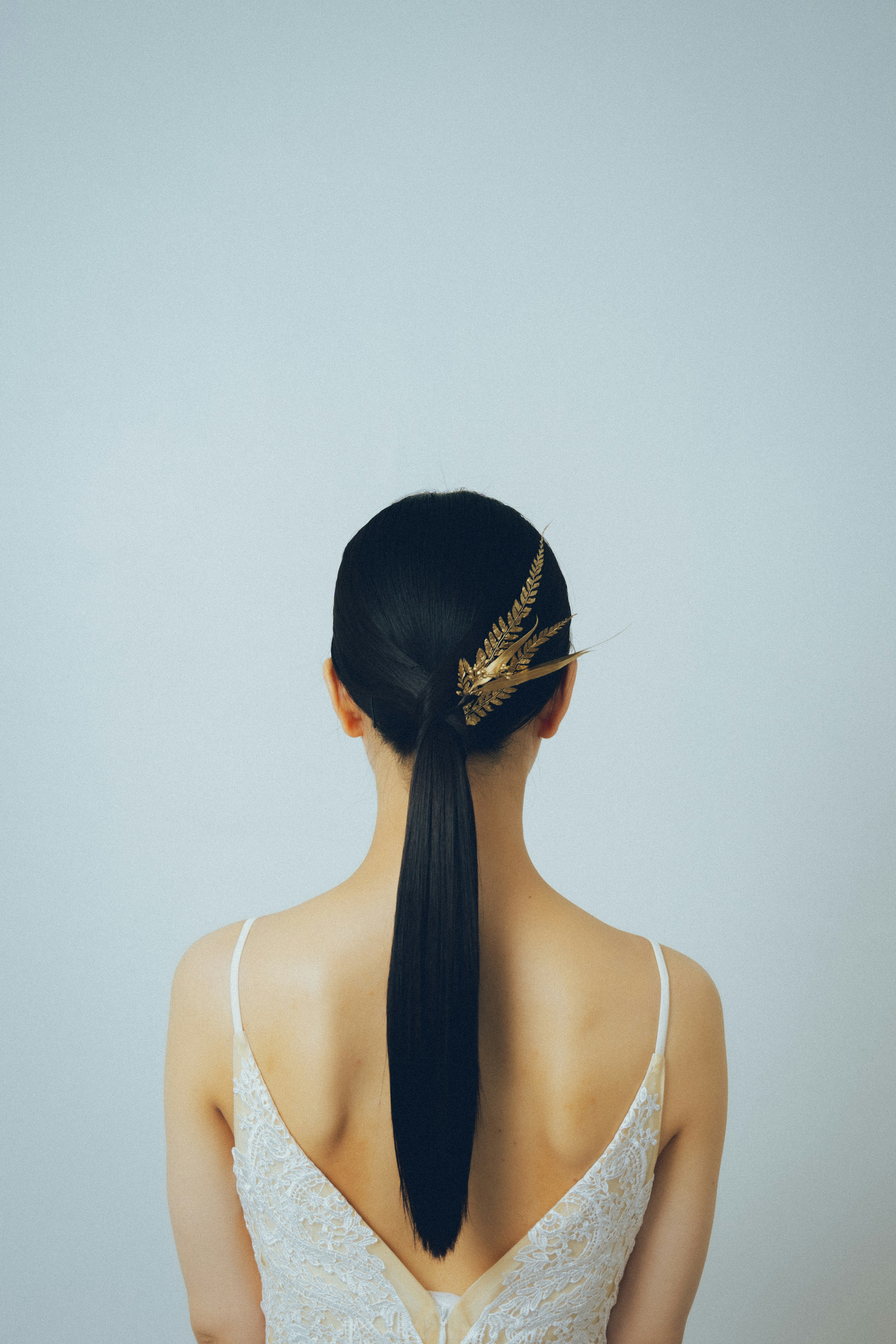 Vista trasera de una mujer con cabello negro liso peinado elegantemente y usando un vestido blanco