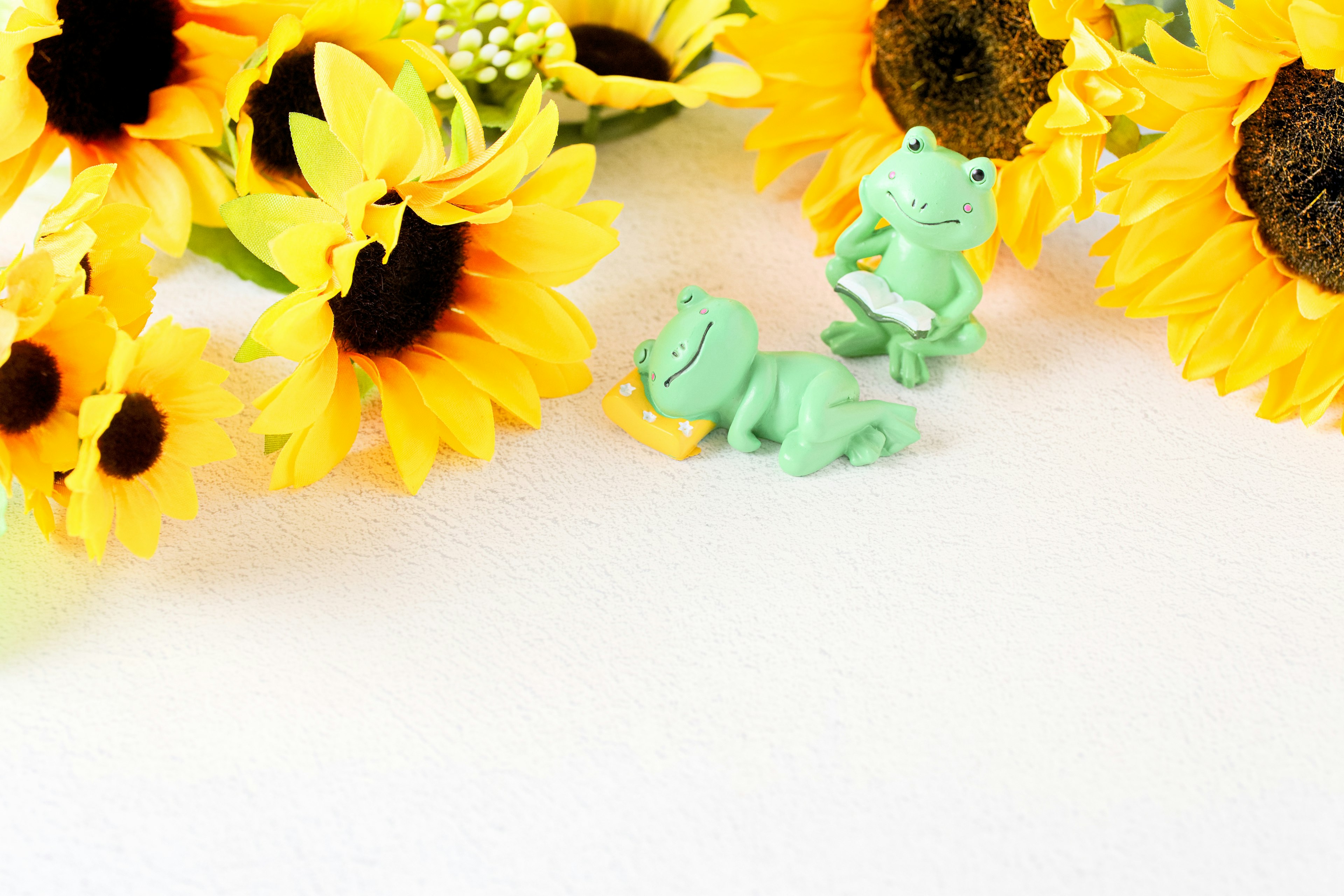 Imagen brillante con dos figuritas de ranas verdes entre girasoles amarillos