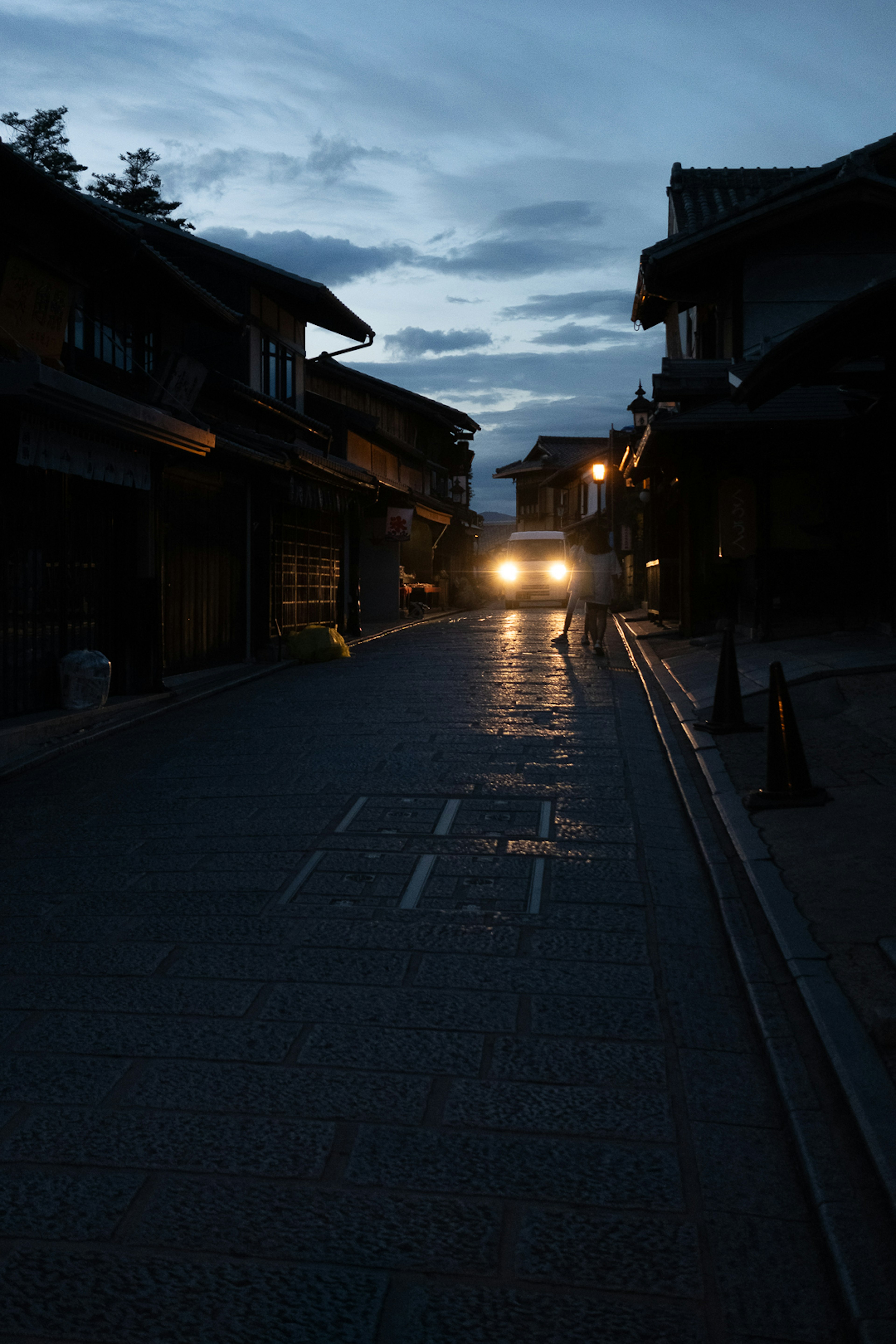 暗い道を照らす車のヘッドライトと周囲の建物