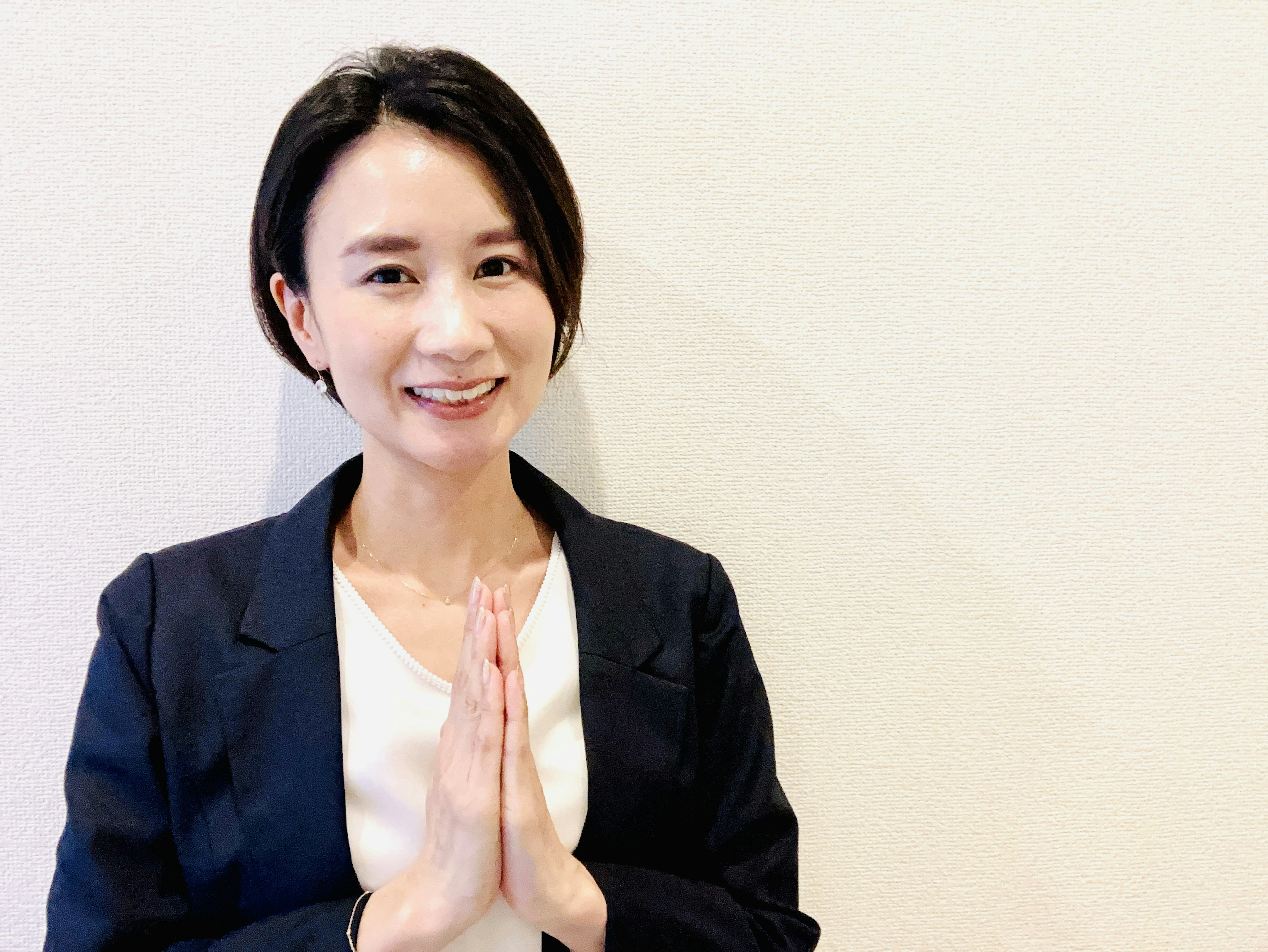 Woman smiling with hands together in front of a white background