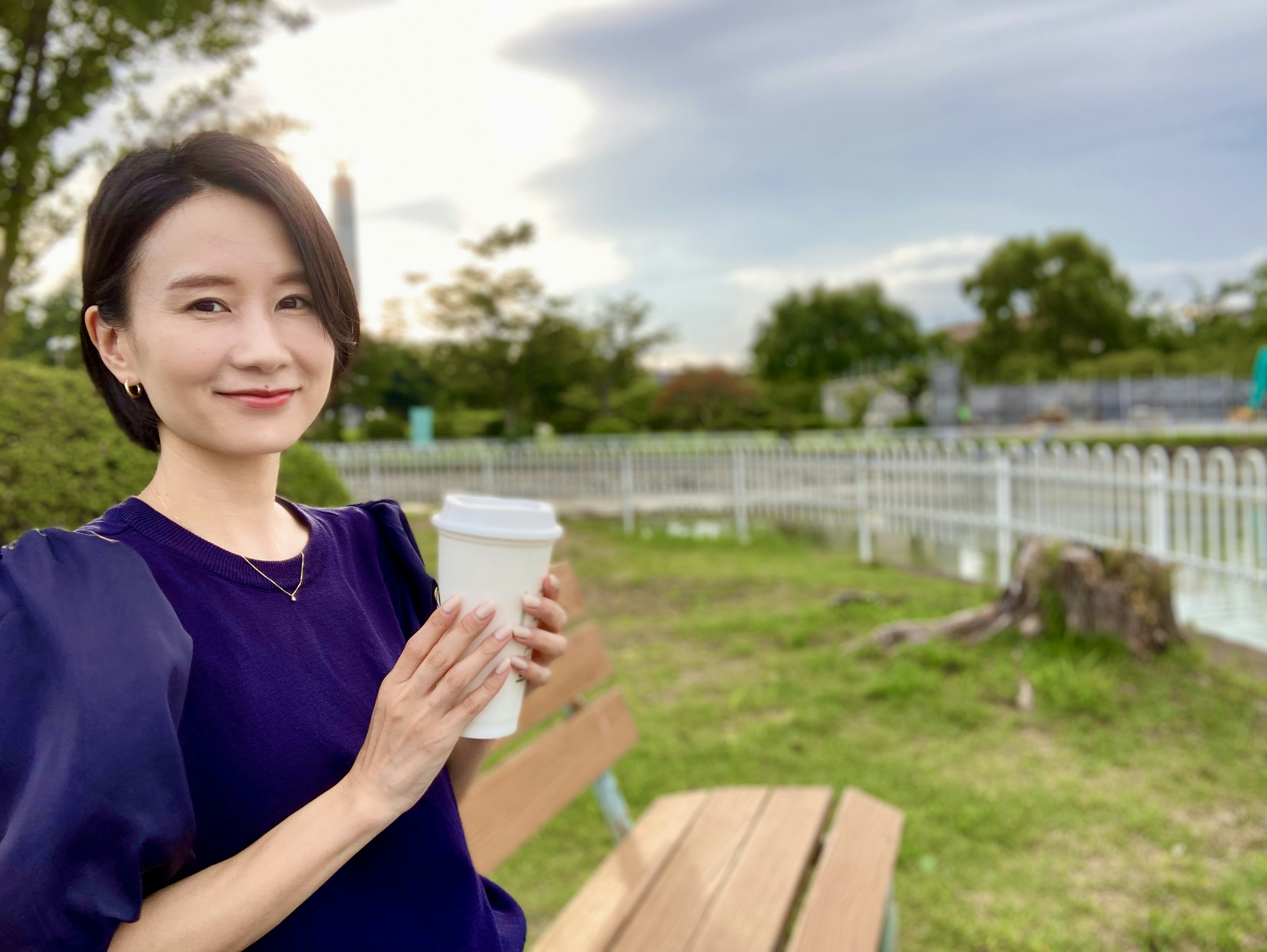 一位女性坐在公園長椅上，手裡拿著咖啡杯，面帶微笑