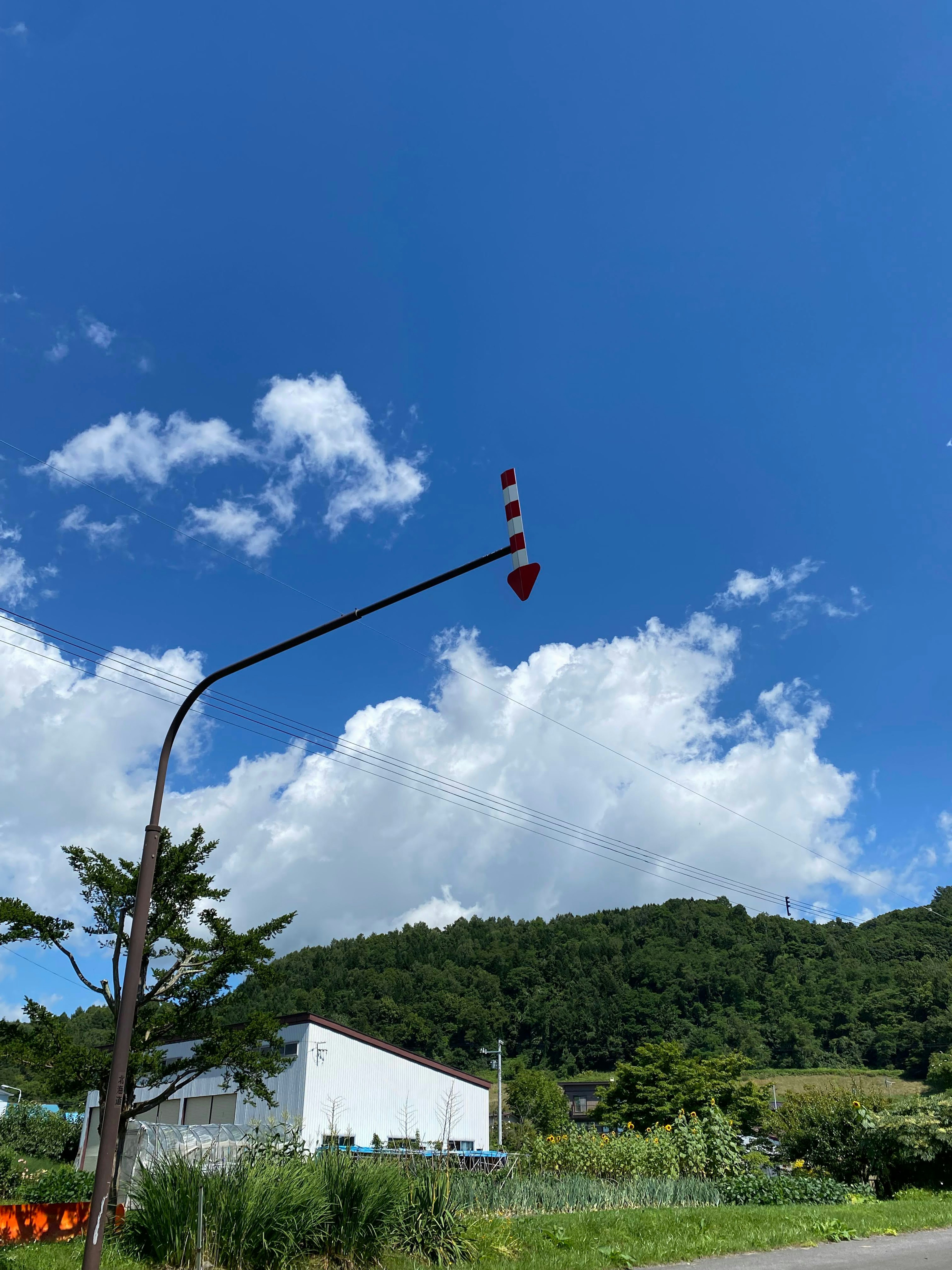 Red arrow sign under a blue sky with clouds and green mountains