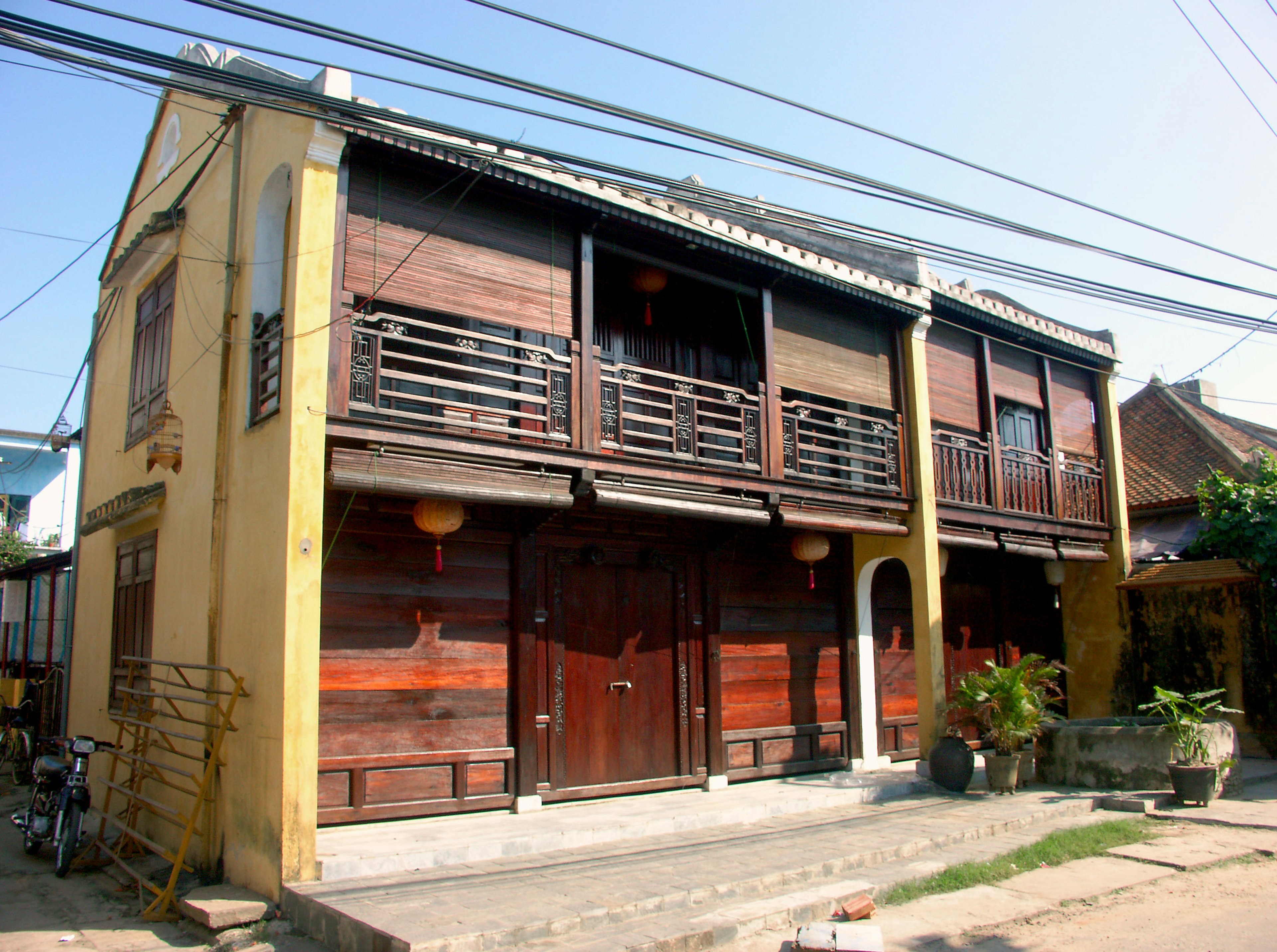 Rumah tradisional kayu dengan eksterior kuning cerah dan balkon kayu