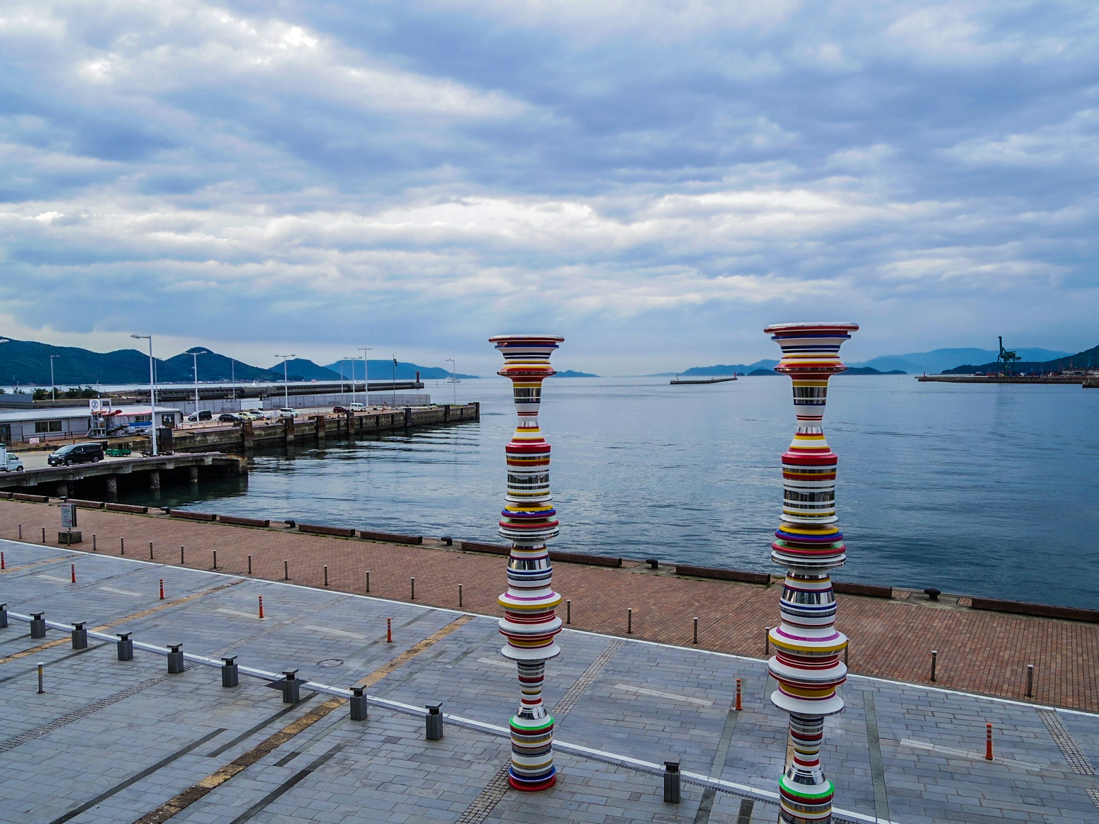 Bunte Säulen stehen am ruhigen Meer unter einem bewölkten Himmel