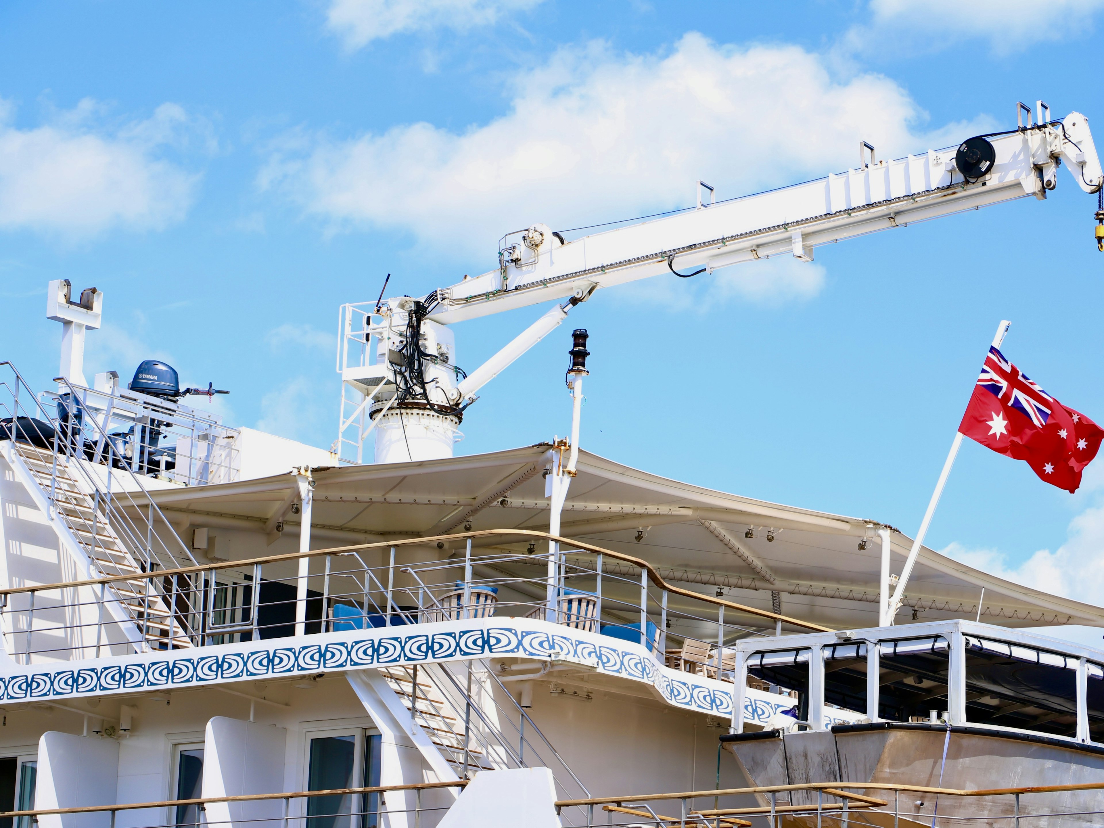 Ein Schiffsdeck mit einem Kran und einer Flagge vor blauem Himmel