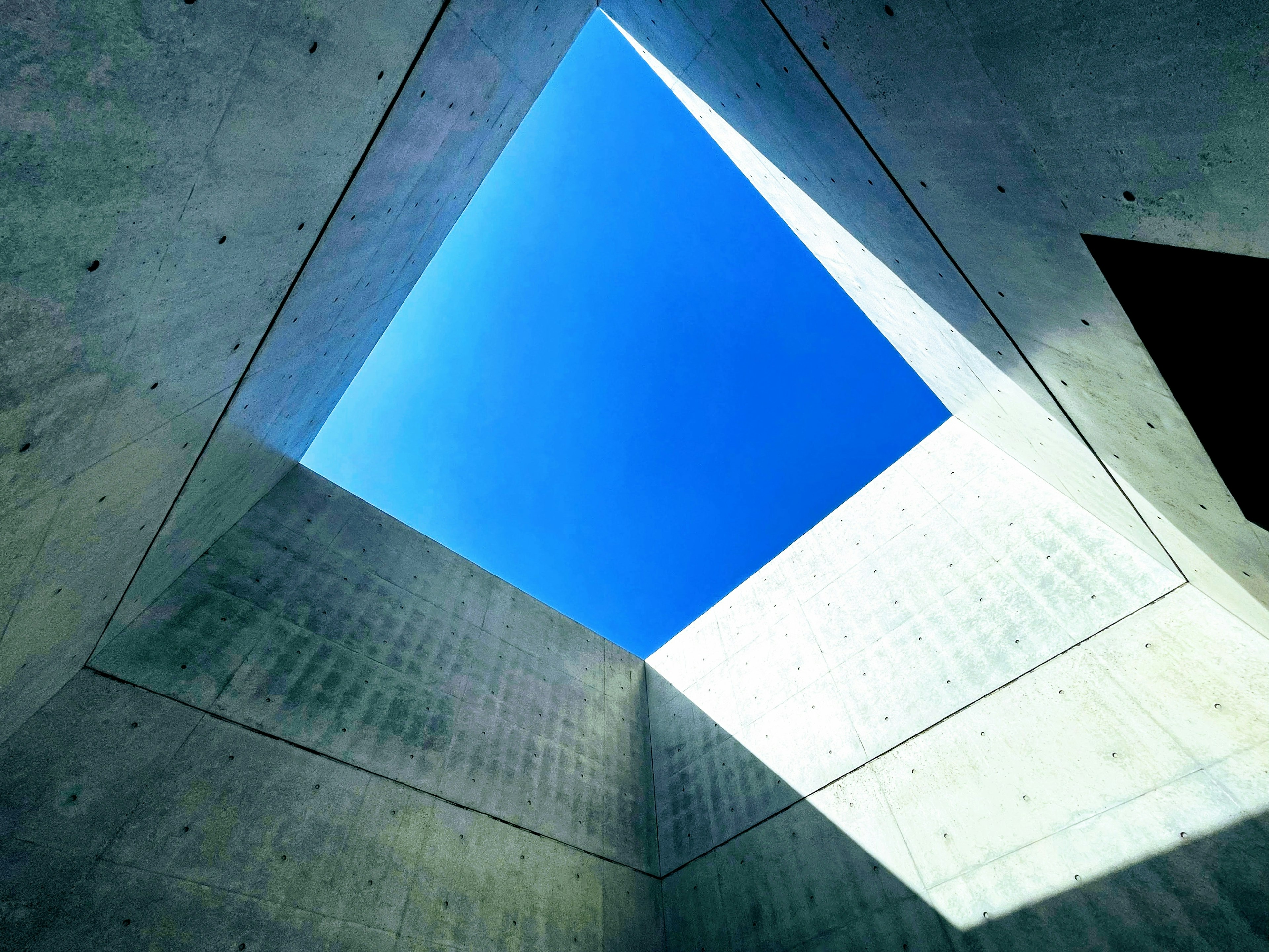 Ventana cuadrada que revela un cielo azul brillante en una estructura de concreto