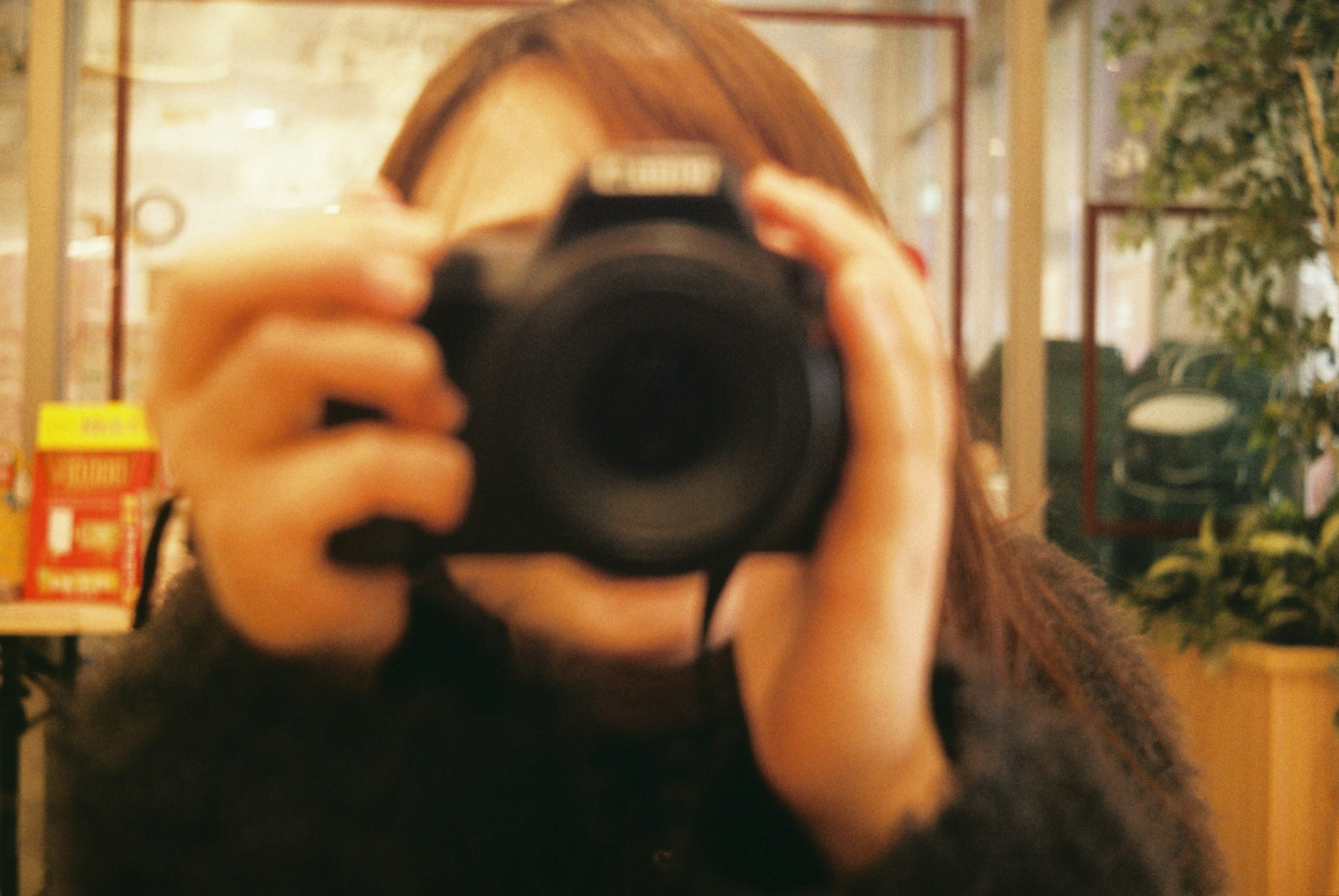 A woman holding a camera with a blurred background in an indoor setting