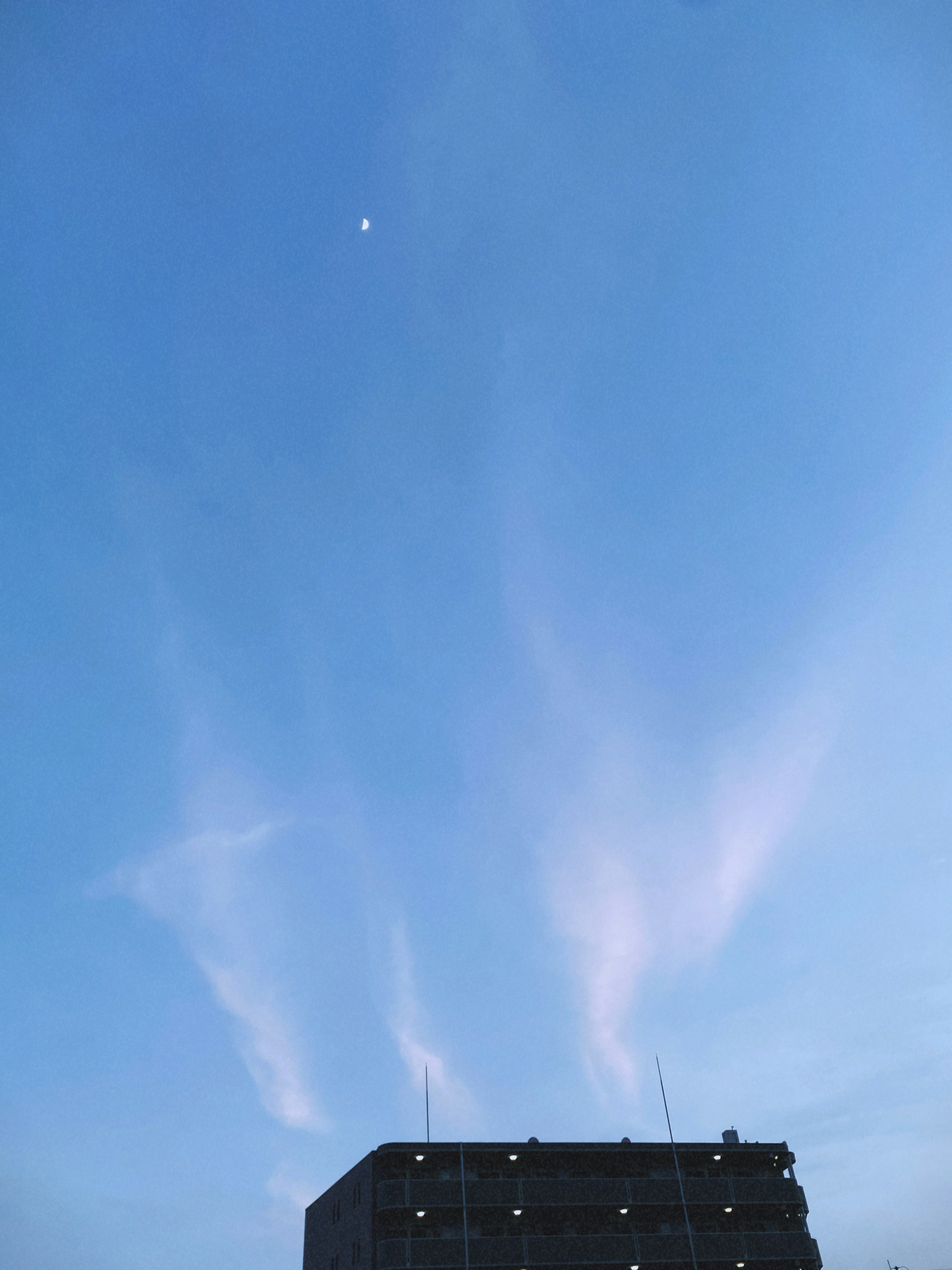 青い空に薄い雲が広がり月が見える夕暮れの風景