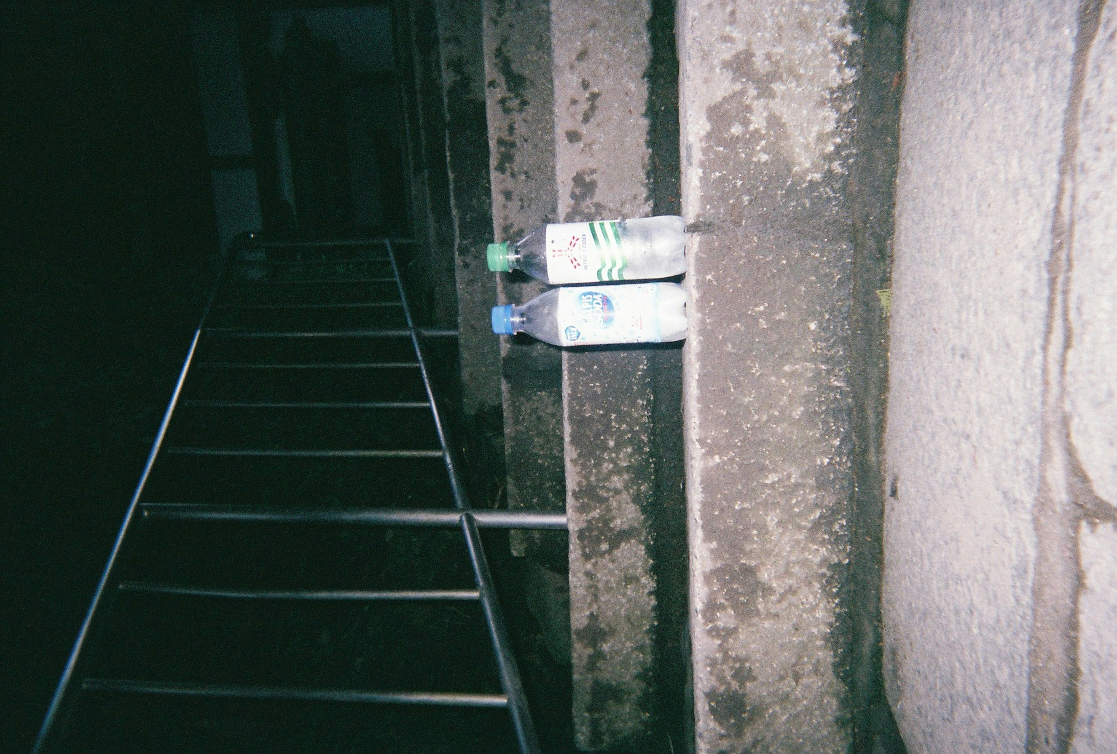 Échelle en métal dans une zone sombre avec deux bouteilles reposant contre un mur humide