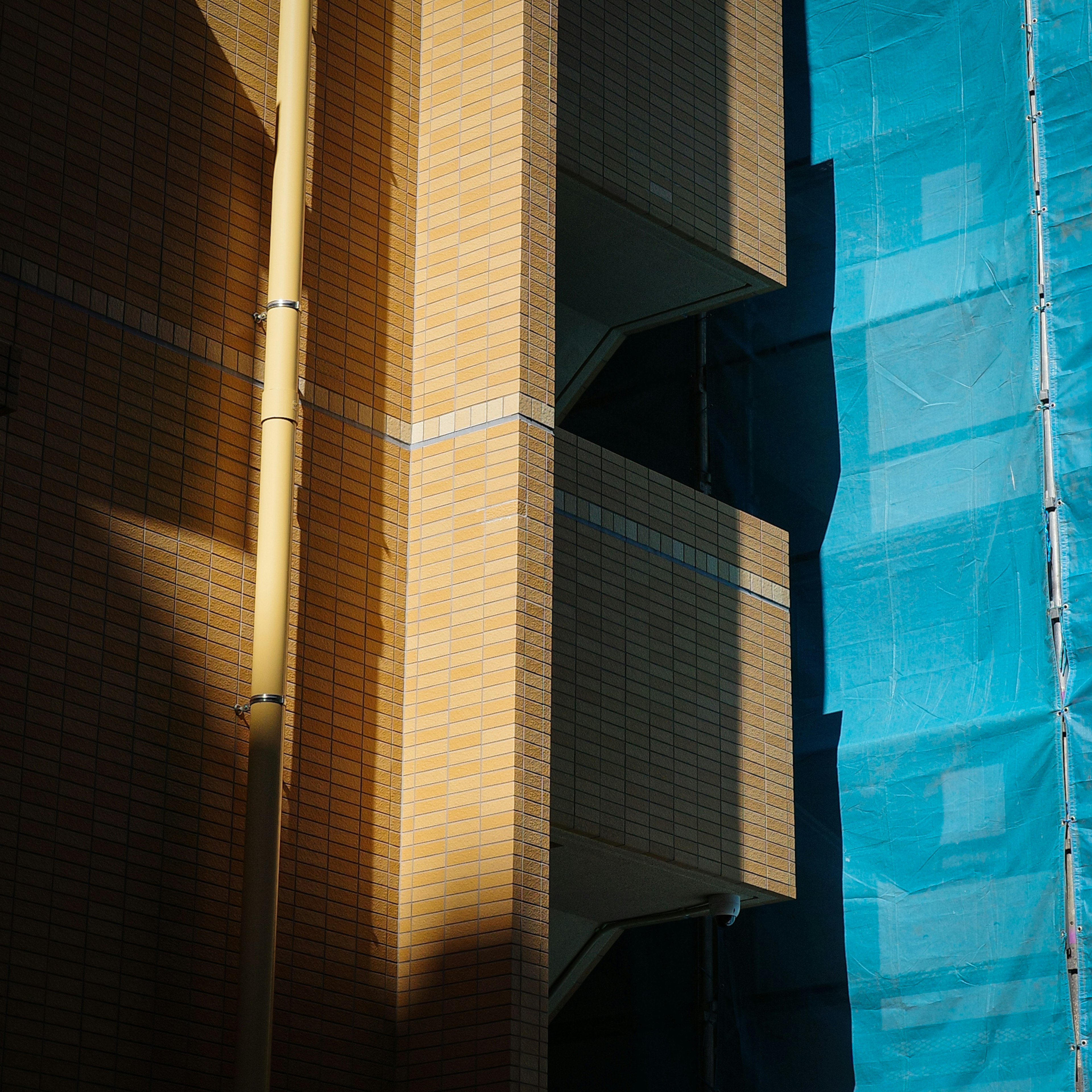 Contrast of shadows on building side and blue tarpaulin