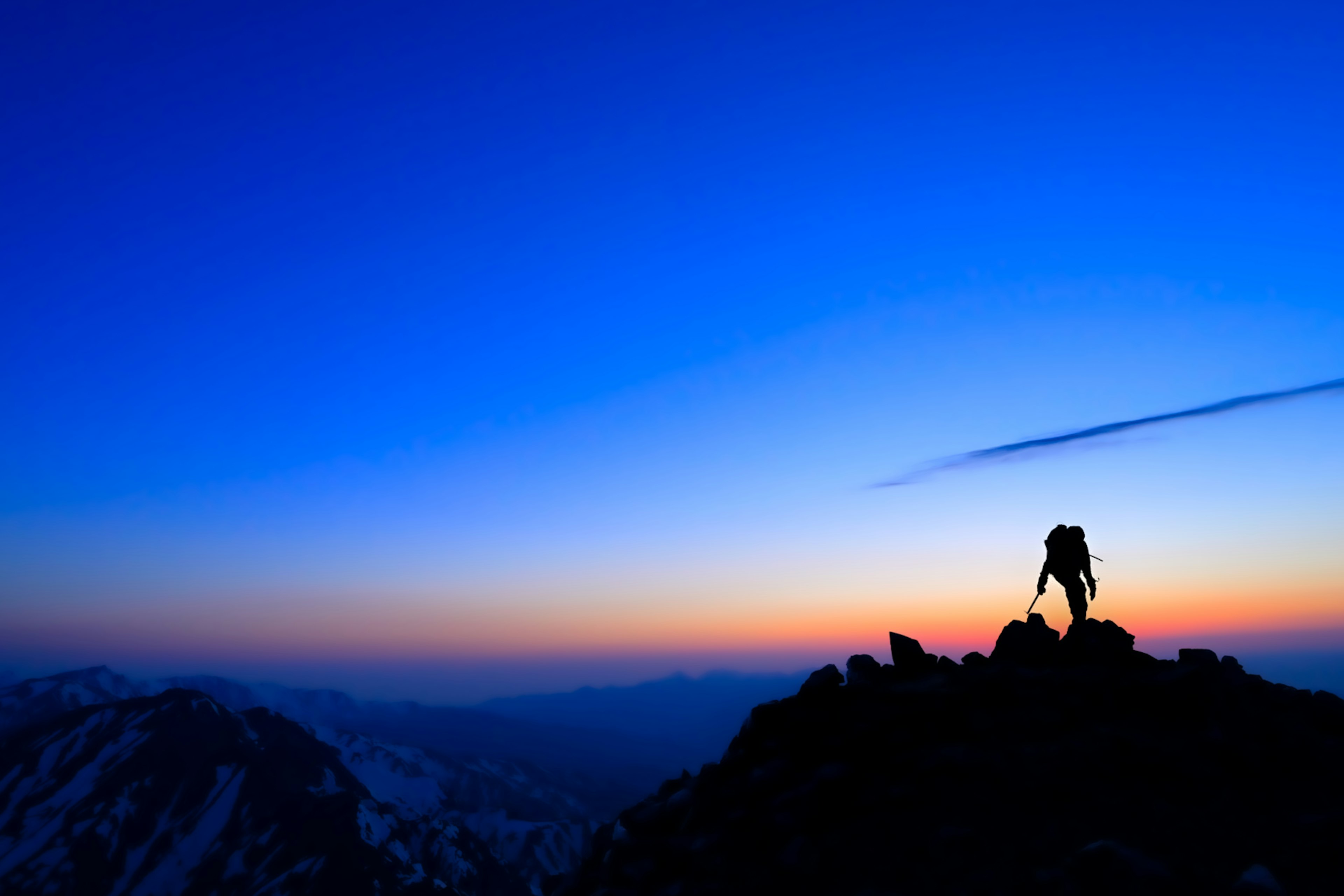 Silueta de un escalador de pie en la cima de una montaña al atardecer