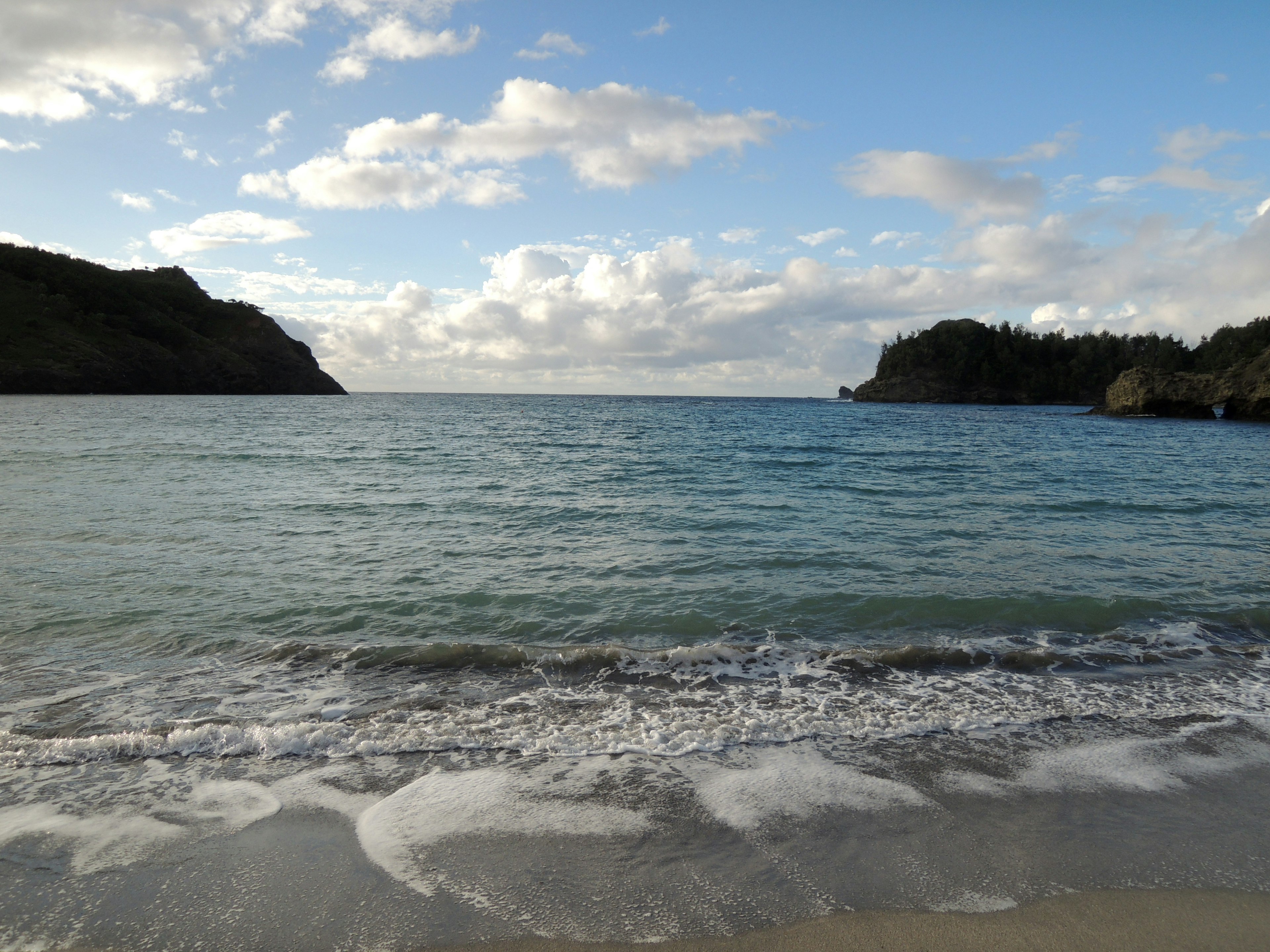 Vue scénique de l'océan bleu et de la plage de sable blanc avec des nuages flottants et des collines