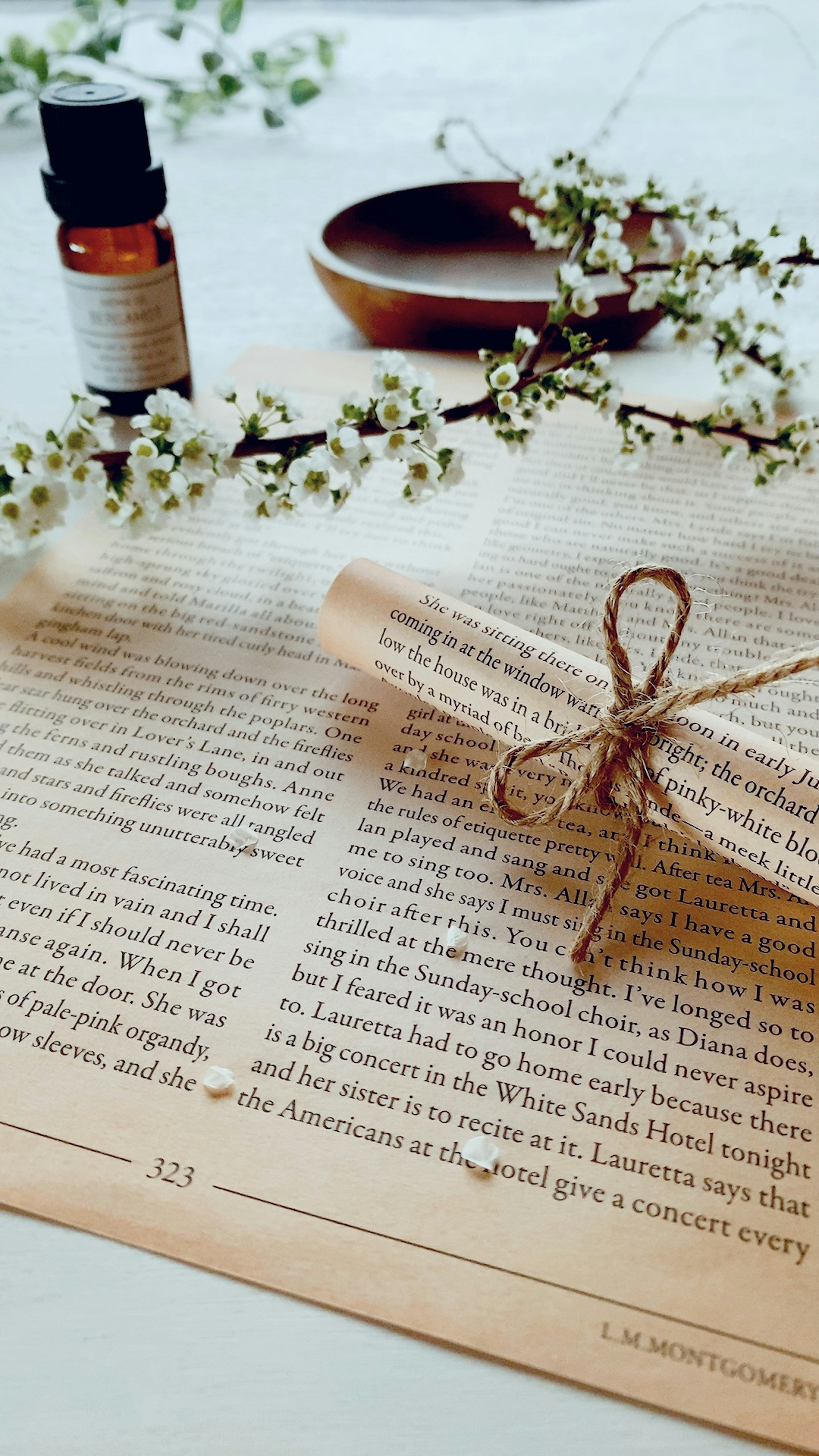 Un rouleau attaché avec de la ficelle sur une page de livre accompagné d'une bouteille d'huile essentielle et de branches florales