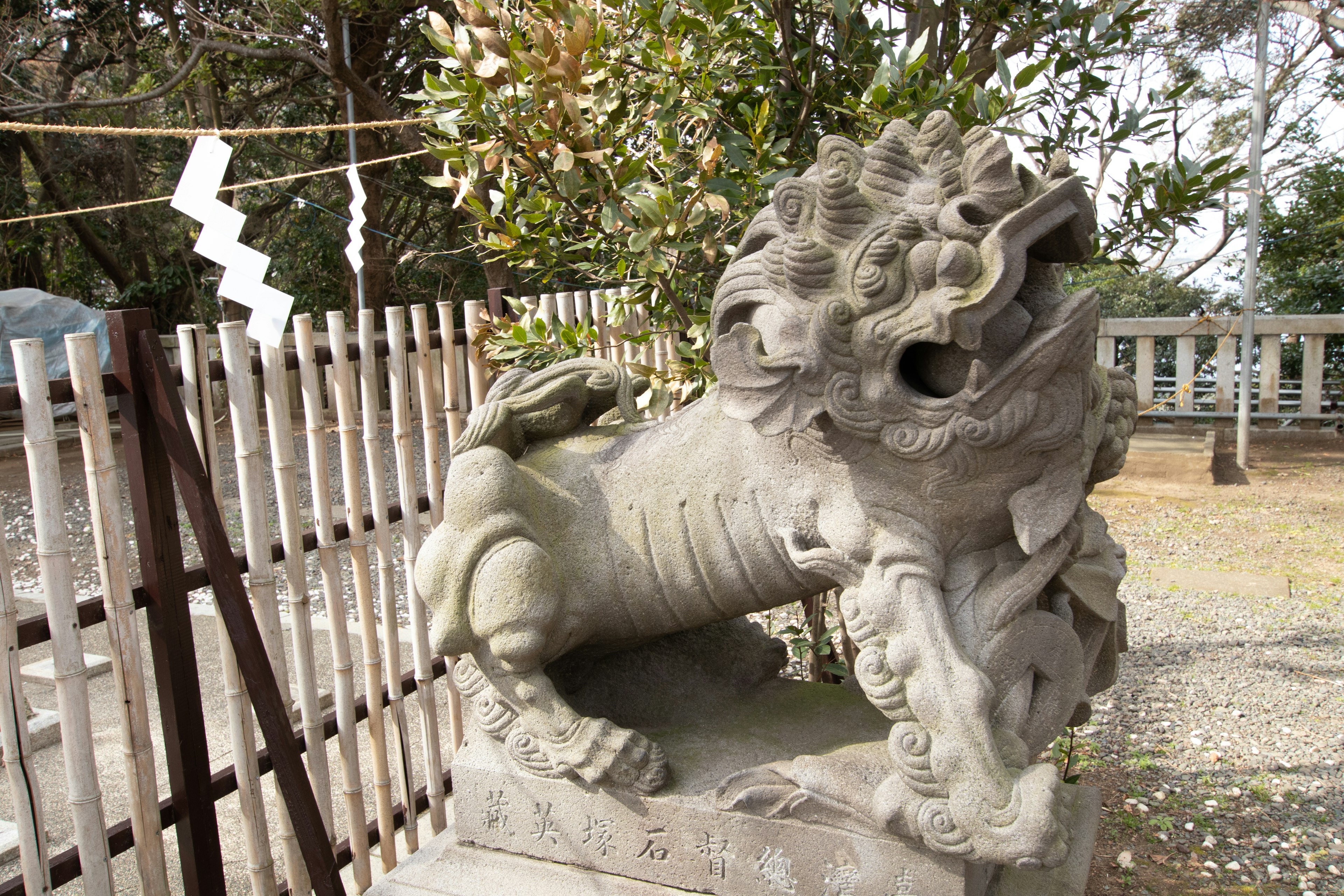 Stone statue of a guardian lion at a shrine with greenery in the background