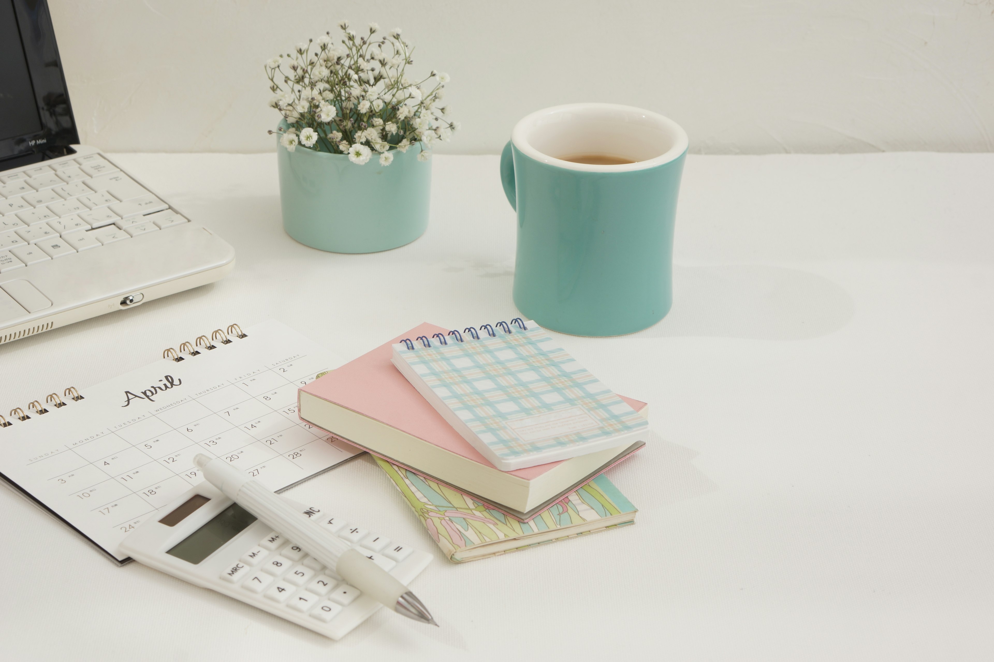 Una tazza blu chiaro con un vaso di fiori una pila di quaderni e un calendario su una scrivania