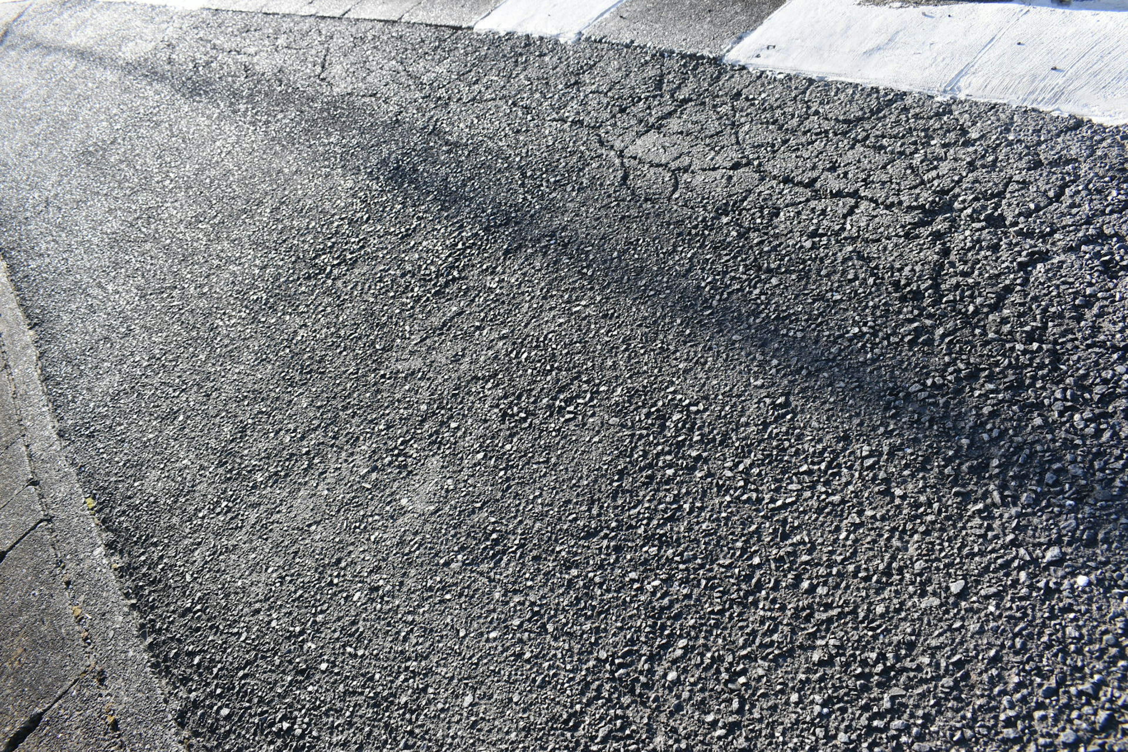 Close-up image of a paved road showing cracked surface and shadow