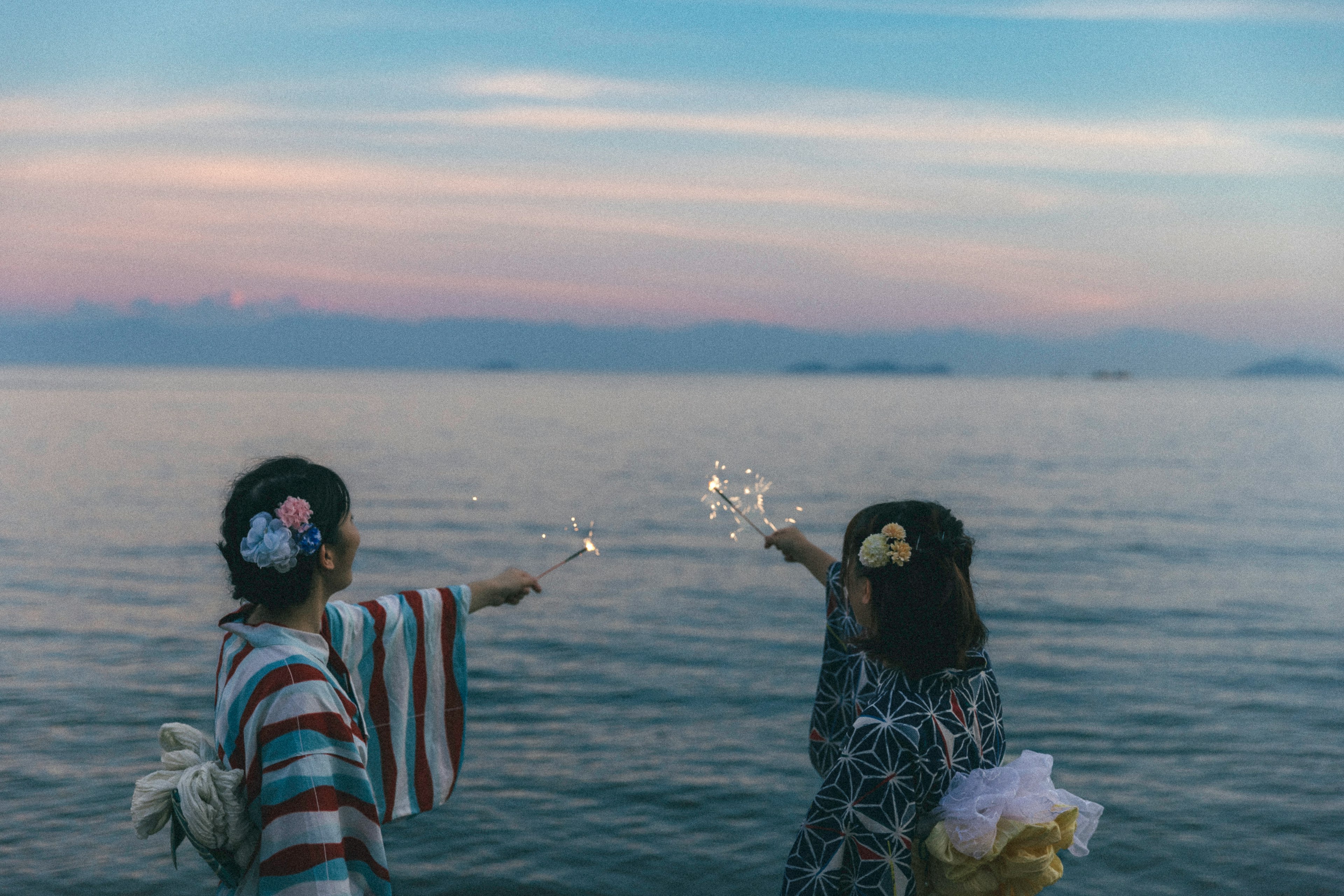 Dos mujeres vestidas con ropa tradicional juegan con burbujas junto al mar al atardecer