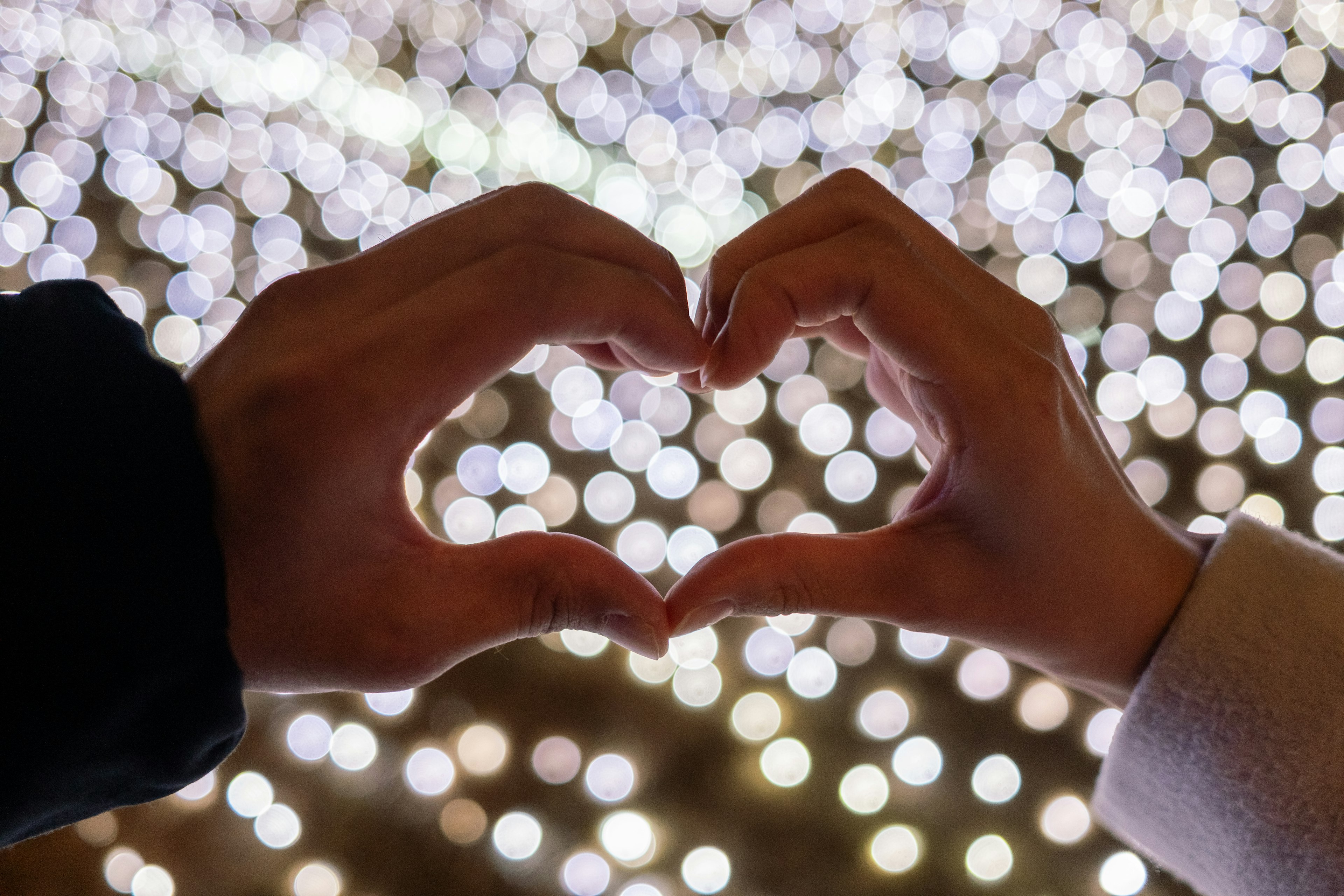 Due mani che formano un cuore su uno sfondo di luci sfocate