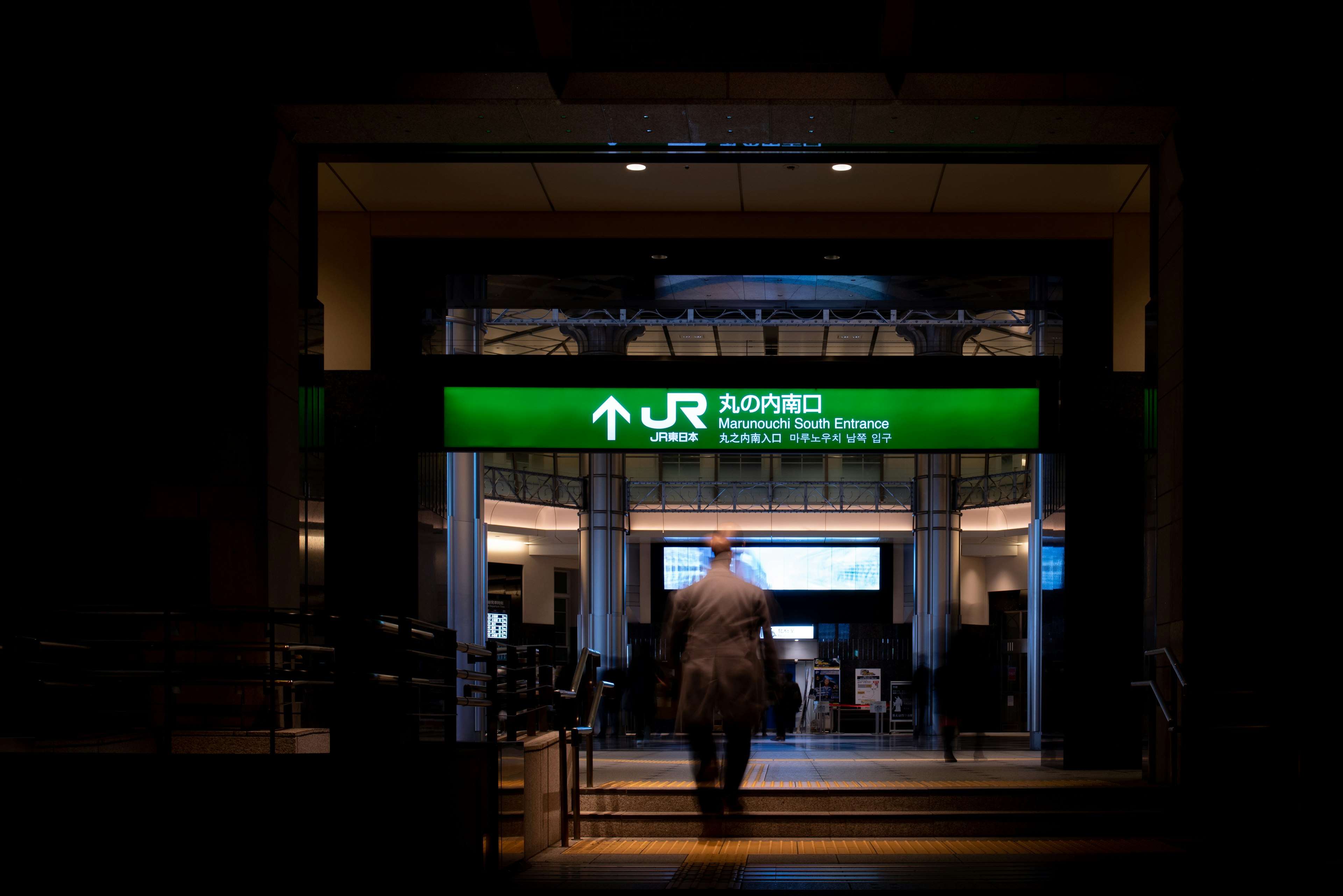 Person walking through an entrance with a bright green sign in a dark environment